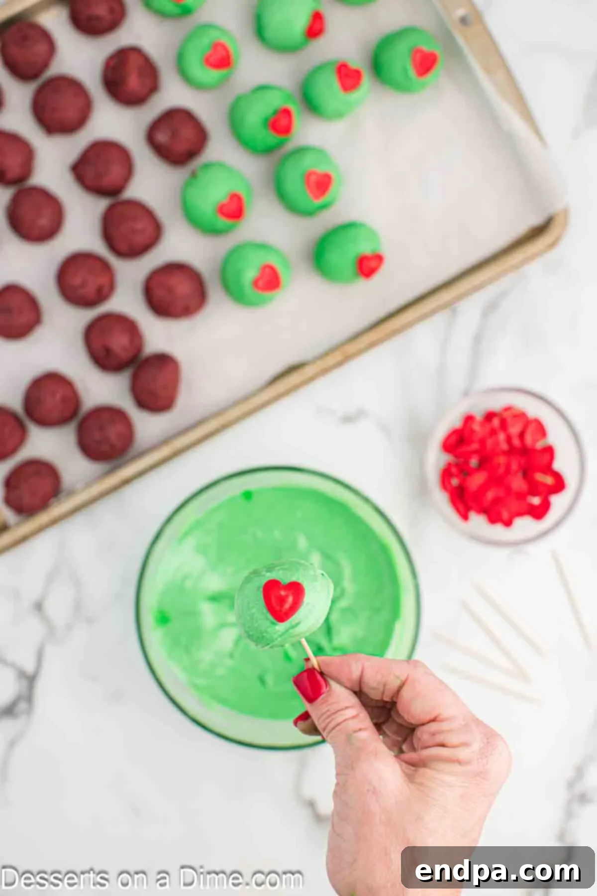 Grinchmas Cake Bites 8 A Grinch Cake Ball with a red heart sprinkle freshly placed on top of the green coating.