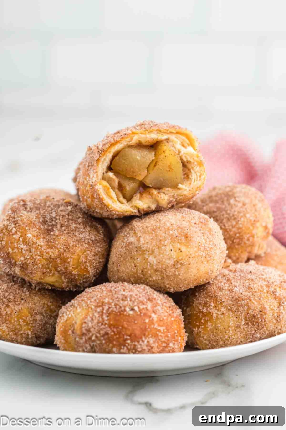 Air Fryer Apple Pie Bites 2 Apple Pie bombs stacked on a plate, golden brown and glistening with cinnamon sugar.