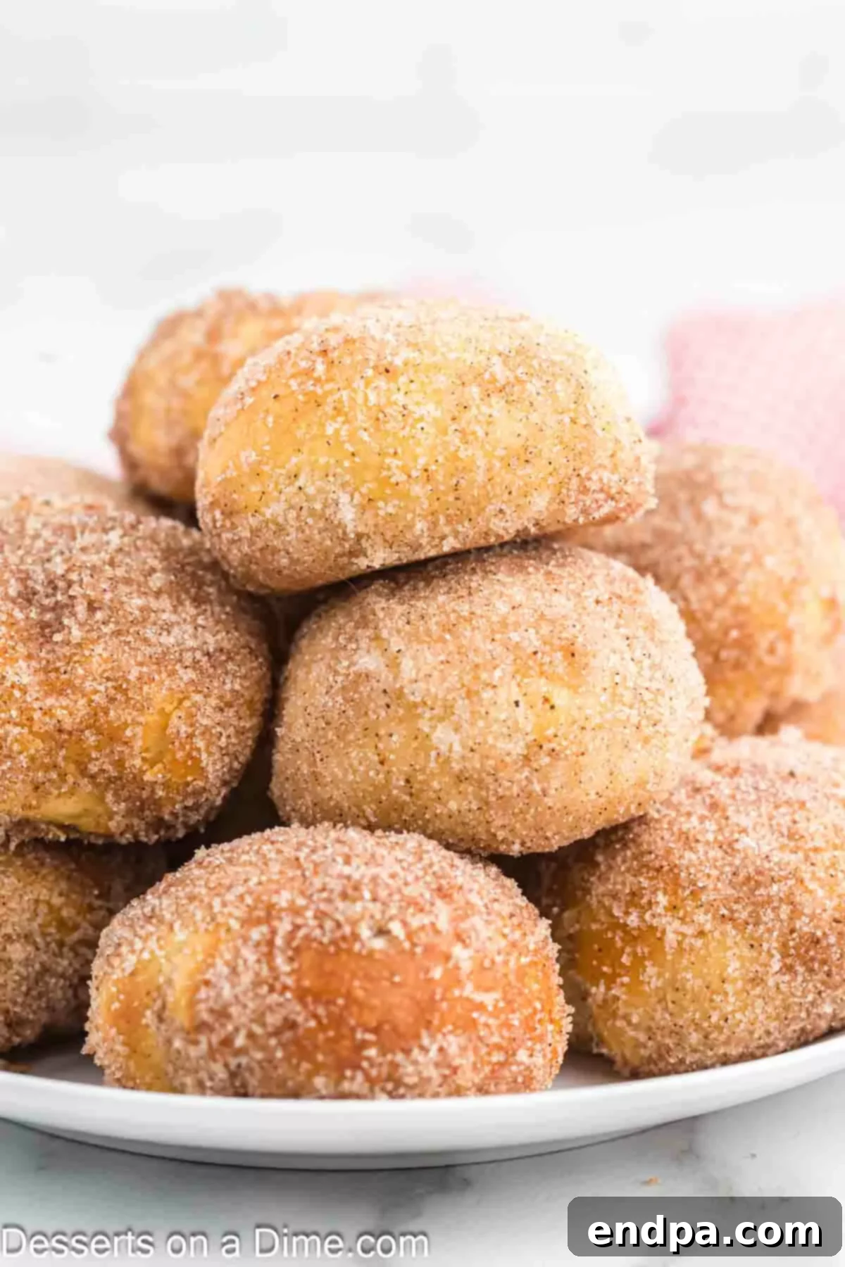 Air Fryer Apple Pie Bites 12 Air Fryer Apple Pie Bombs, glistening with cinnamon sugar, stacked invitingly on a white plate.