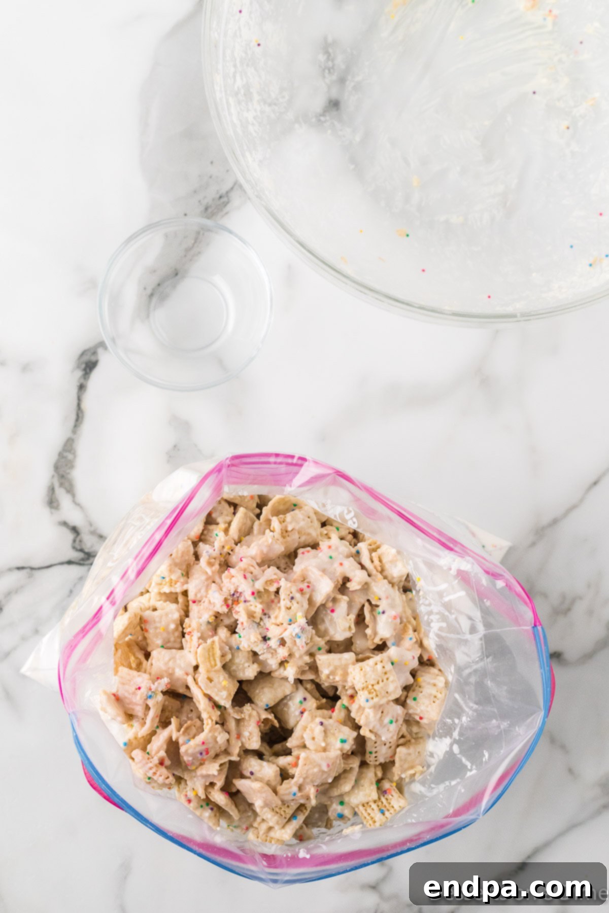Festive Funfetti Snack Mix 8 Chocolate-coated Chex mix being poured into a large ziplock bag containing Funfetti cake mix