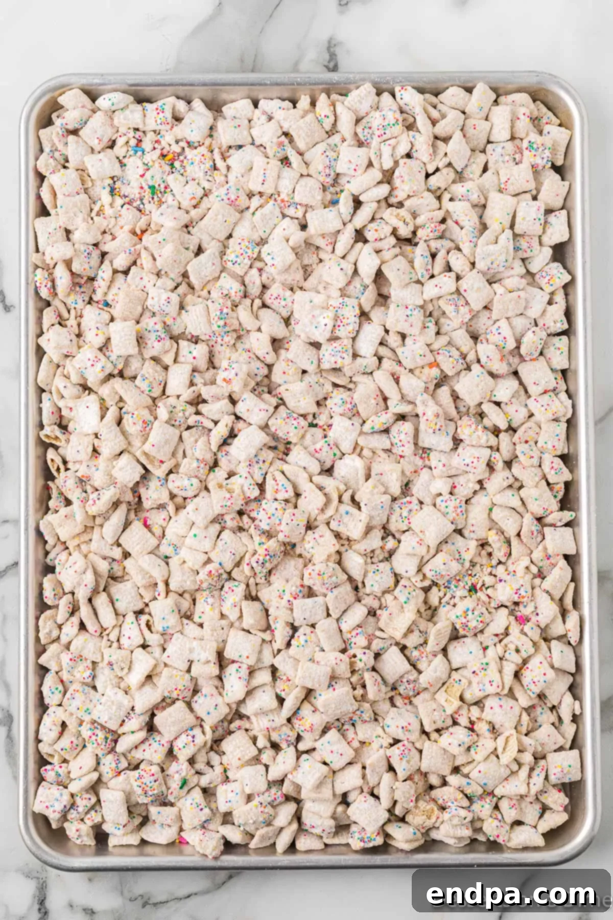 Festive Funfetti Snack Mix 9 The freshly coated Funfetti Puppy Chow spread out on a baking sheet lined with parchment paper