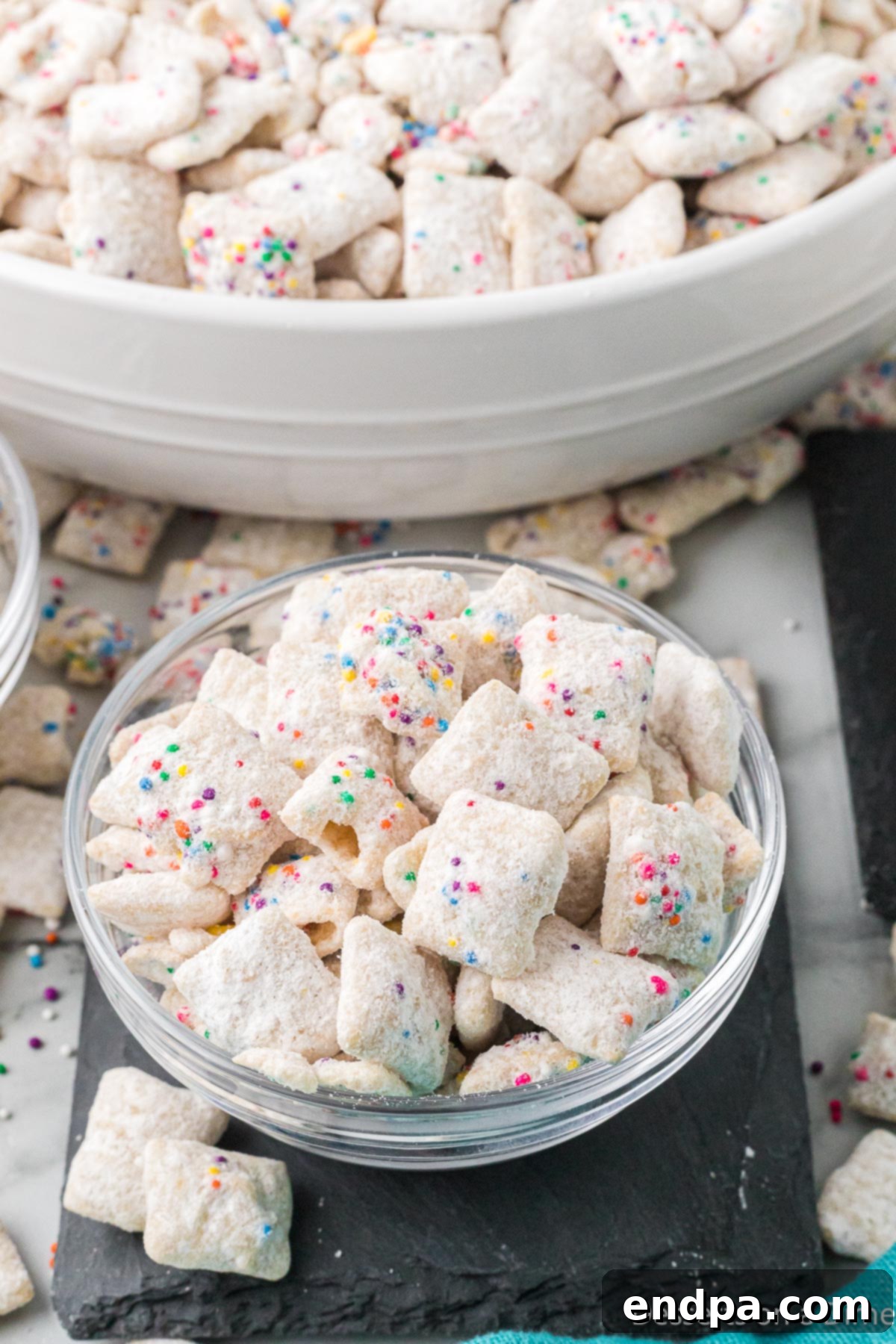 Festive Funfetti Snack Mix 10 A clear glass bowl filled with colorful Funfetti Puppy Chow, showcasing its vibrant sprinkles and powdery coating