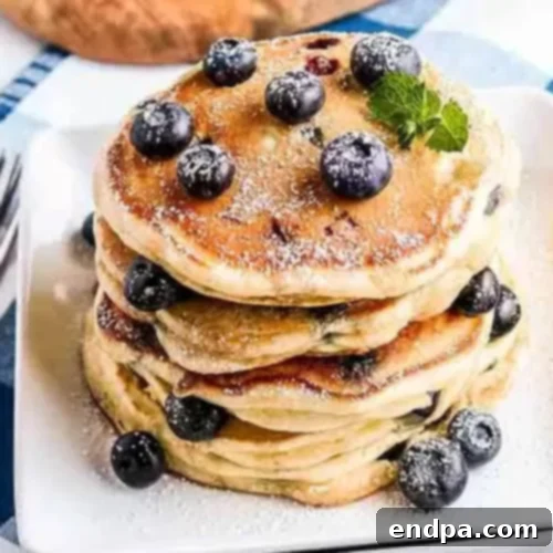 Stack of fluffy Blueberry Pancakes topped with fresh blueberries and maple syrup.