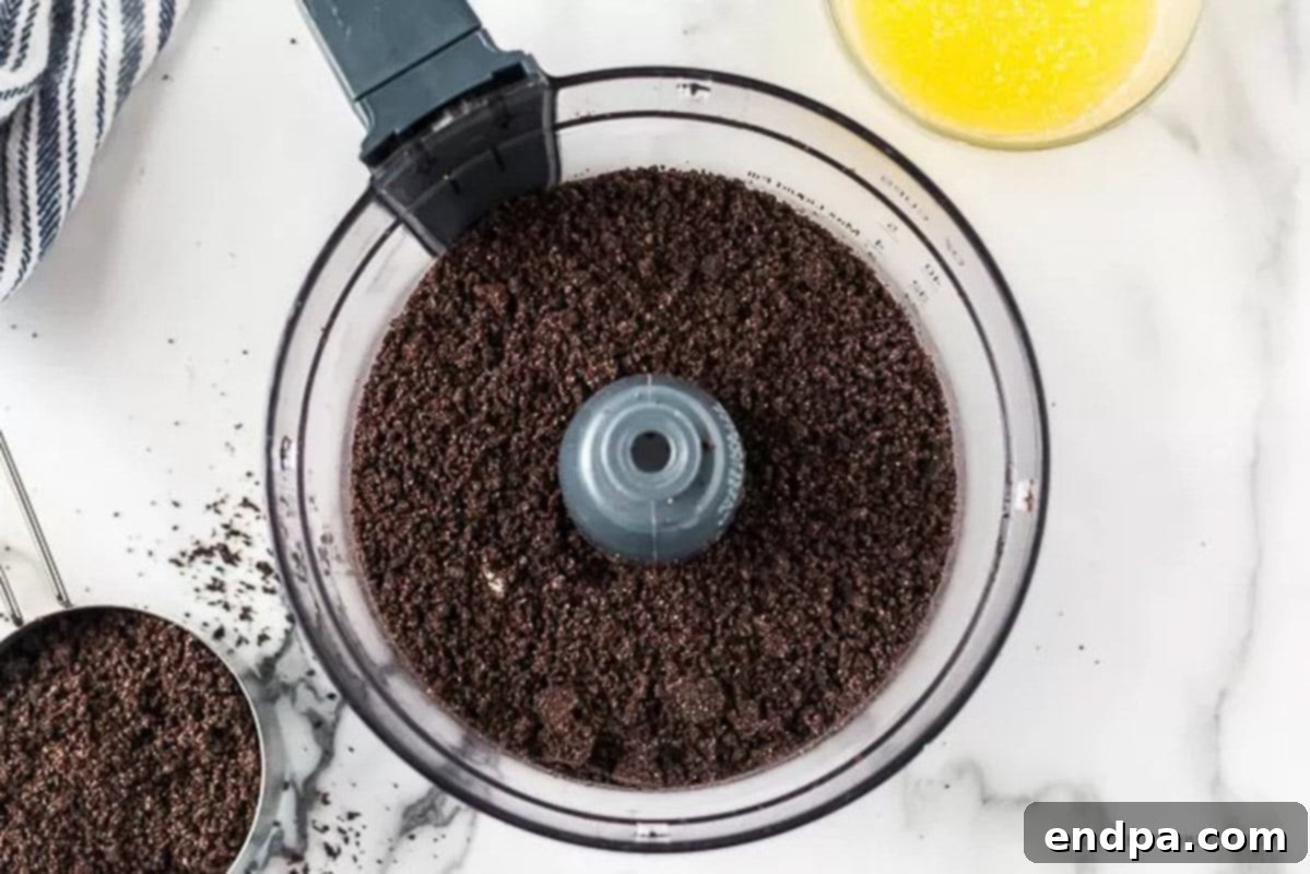 Oreo cookies being crushed in a food processor to create fine crumbs for the crust.