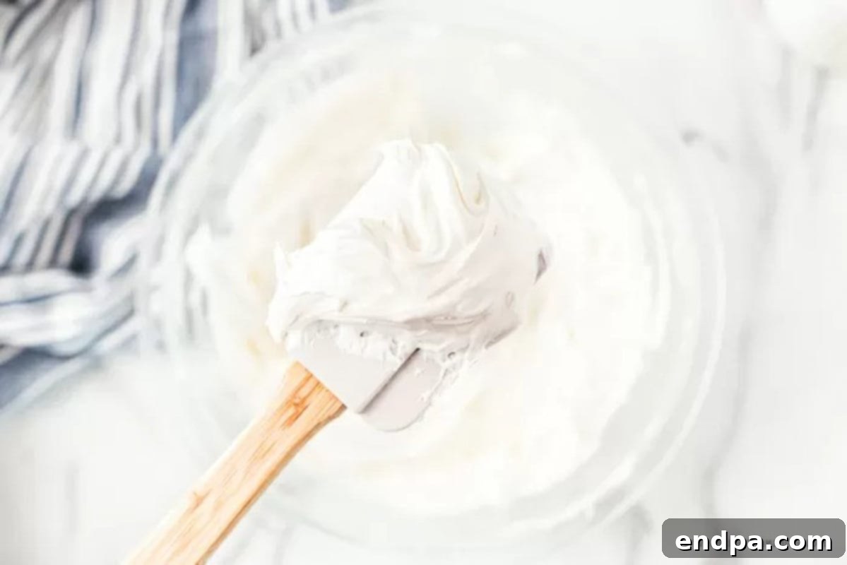 A mixing bowl containing the creamy cream cheese layer, a blend of softened cream cheese, powdered sugar, and half of the Cool Whip.