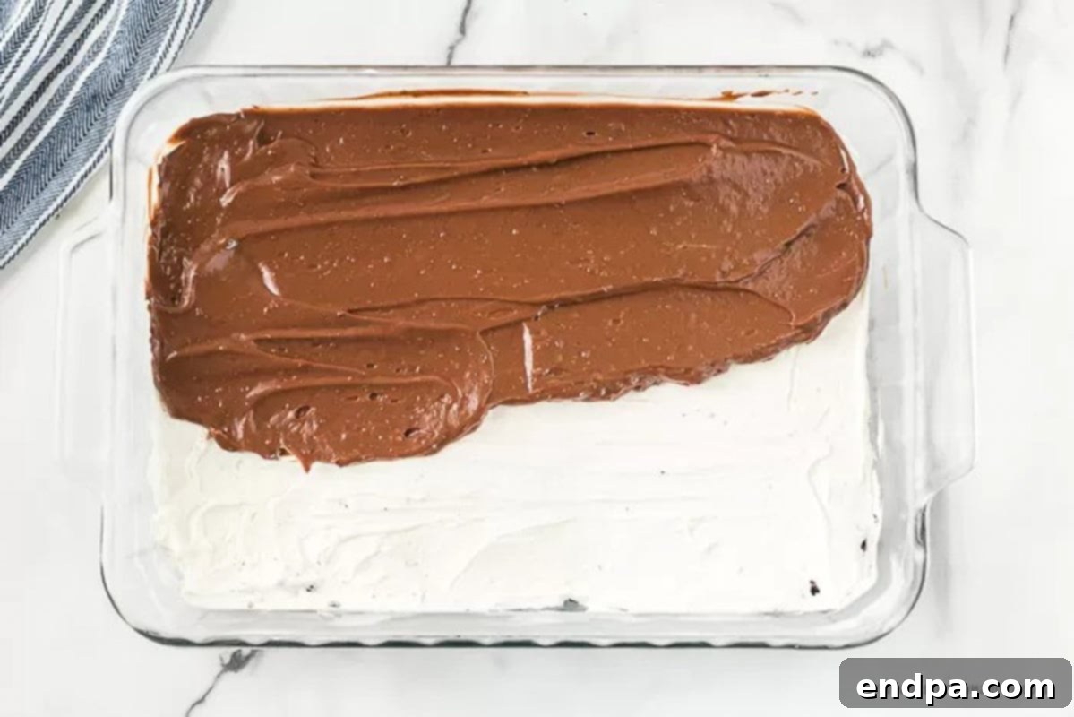 The thickened chocolate pudding layer being carefully spread over the cream cheese filling in the baking dish.