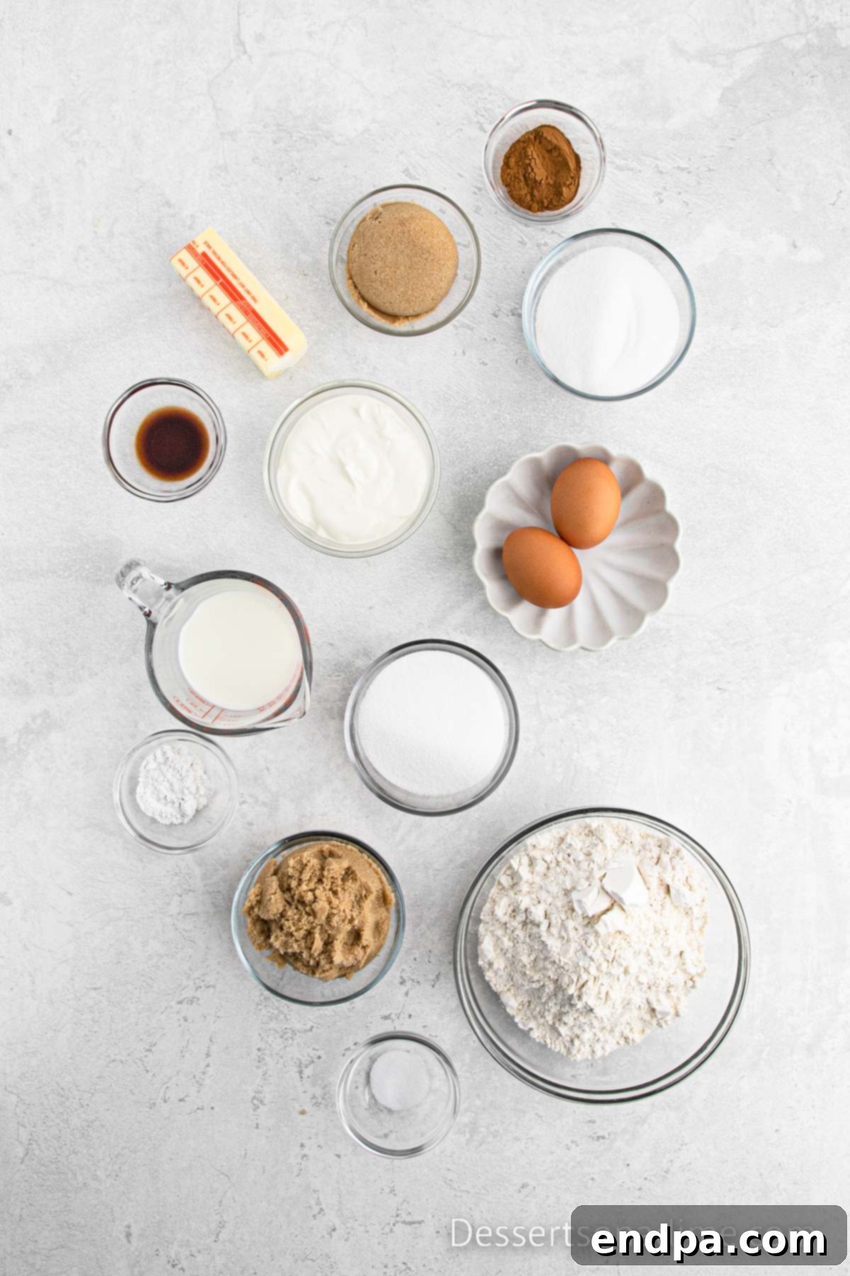A collection of fresh ingredients for cinnamon swirl bread, including flour, cinnamon, sugar, butter, vanilla extract, eggs, milk, and sour cream.