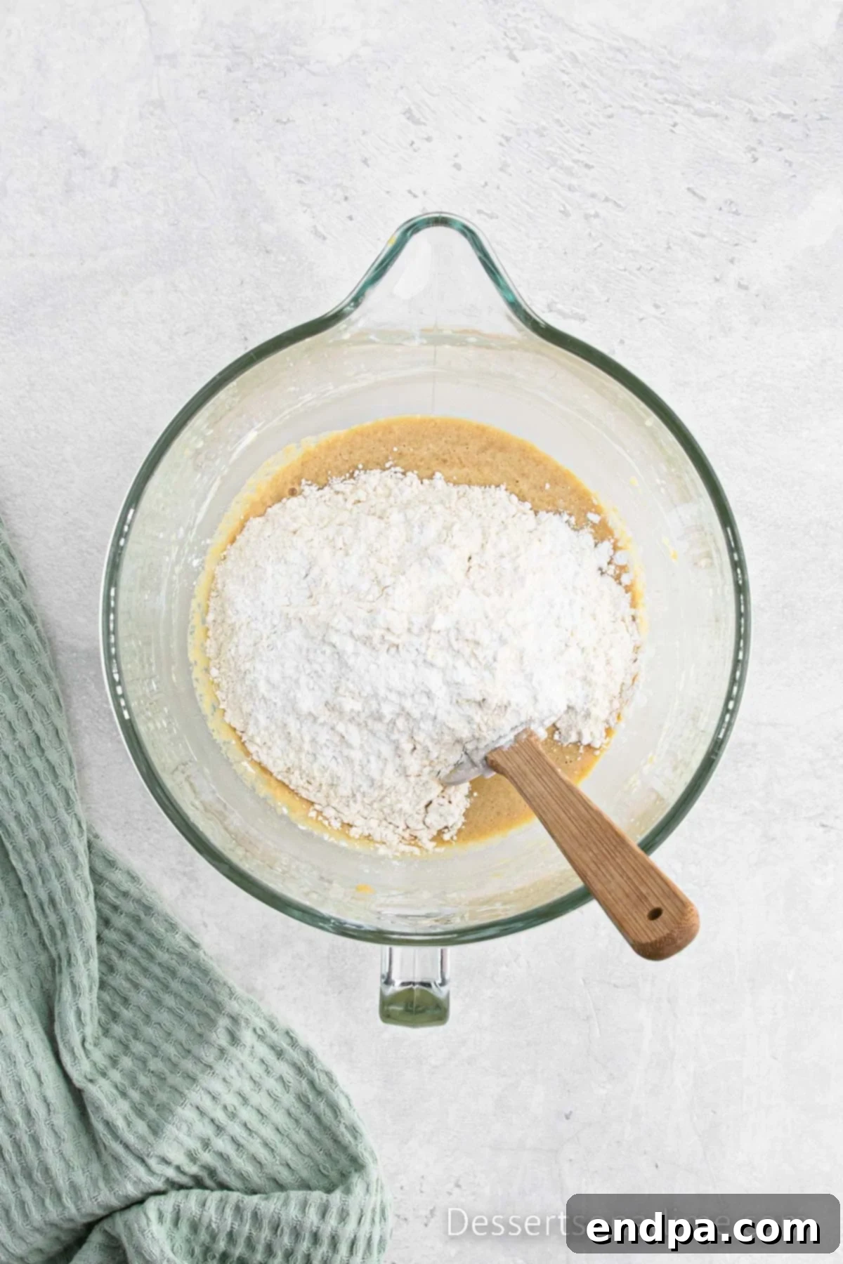 Mixer bowl showing dry ingredients (flour, baking powder, salt) being gently folded into the wet batter.