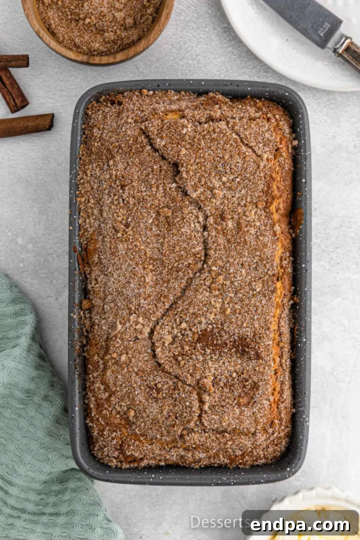 Freshly baked snickerdoodle bread in a loaf pan, with a beautifully cracked cinnamon sugar topping.