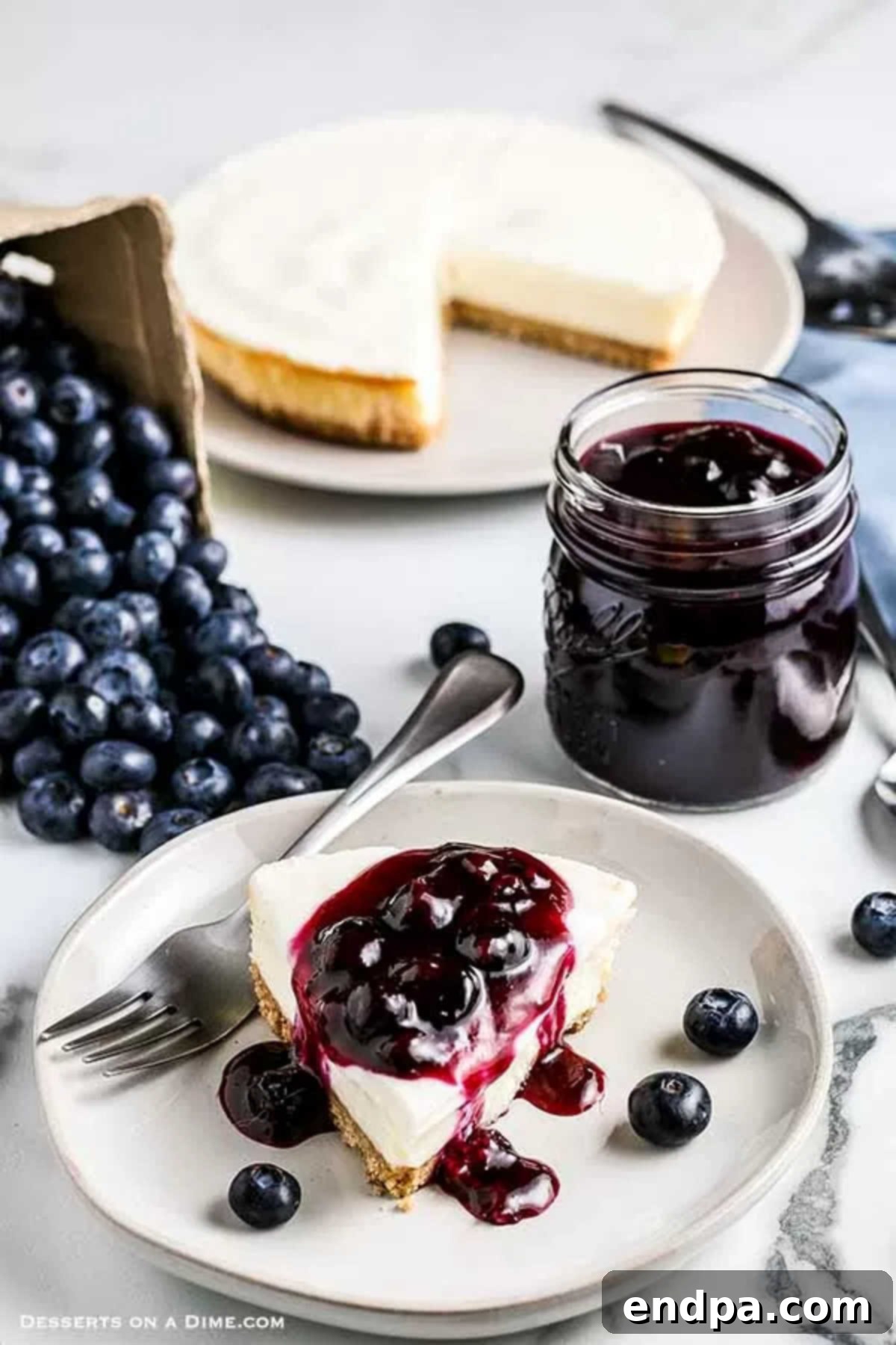 Close up image of blueberry sauce in a mason jar with a slice of cheesecake with blueberry sauce on top