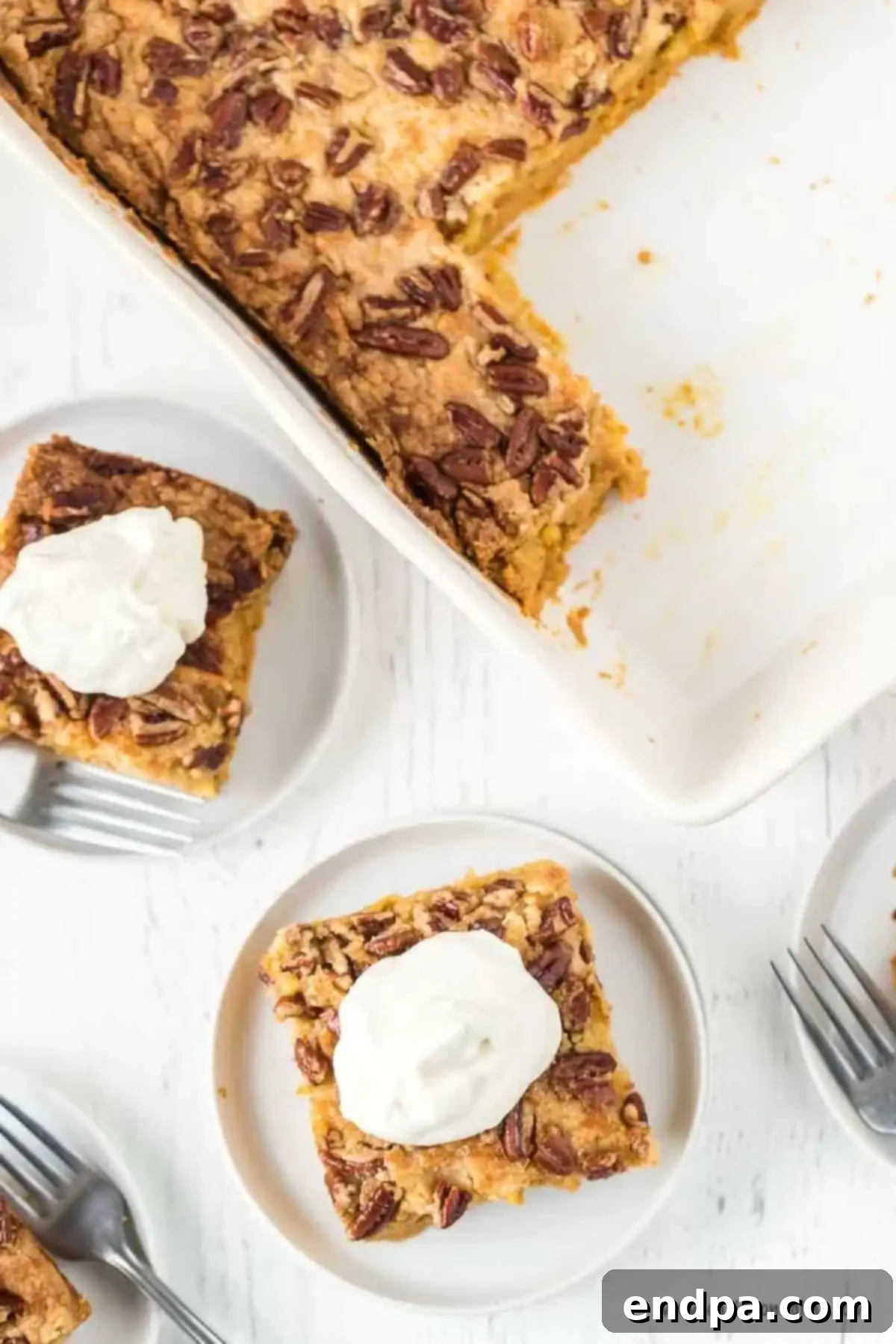 A serving of pumpkin dump cake on a white plate, with the entire dump cake in the background. The cake is golden brown with a creamy pumpkin layer.