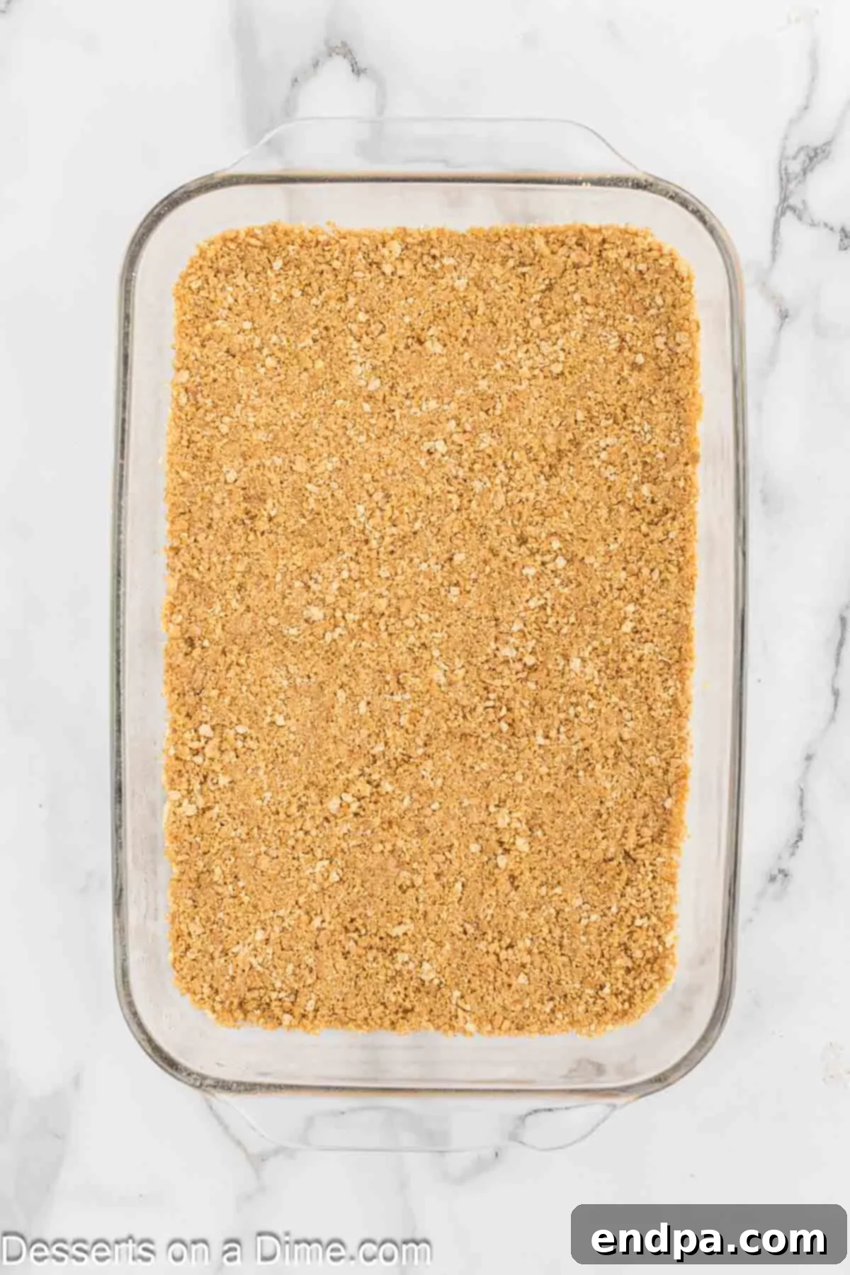 Banana Split Dream Cake 2 Crushed graham cracker crumbs pressed into a 9x13 inch baking dish, forming the base of the no-bake cake.