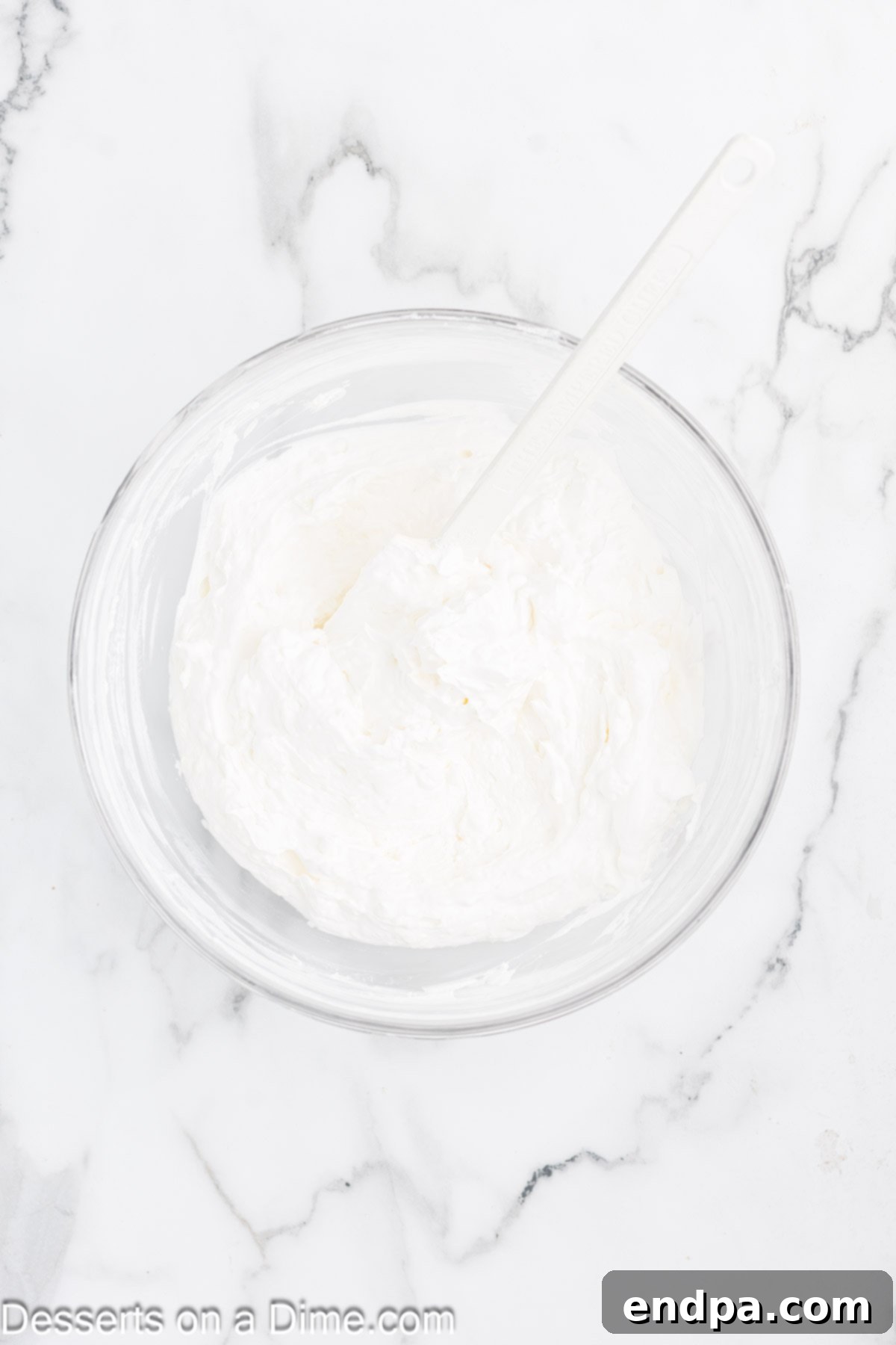 Banana Split Dream Cake 3 Cream cheese mixture being whipped in a medium bowl with an electric mixer, appearing light and fluffy.