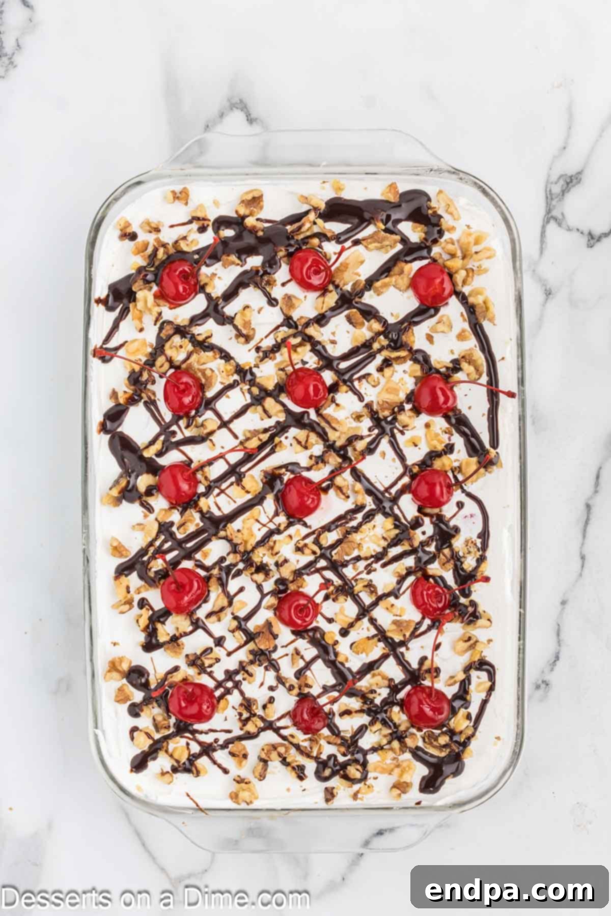 Banana Split Dream Cake 7 The finished No Bake Banana Split Cake, topped with a smooth layer of whipped cream, drizzled with chocolate syrup, sprinkled with walnuts, and garnished with bright maraschino cherries.