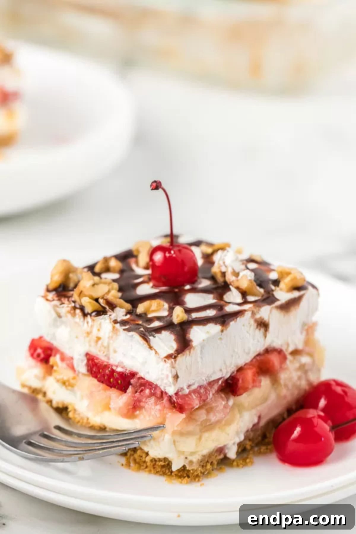 No bake banana split cake recipe is easy and always a hit. Layers of strawberries, crushed pineapple and more topped with chocolate make this one of the best no bake desserts. Everyone will enjoy banana split cake no bake recipe. #dessertonadime #bananasplitcake Another mouth-watering slice of No Bake Banana Split Cake, showcasing its beautiful layers and tempting toppings, ready to be enjoyed.