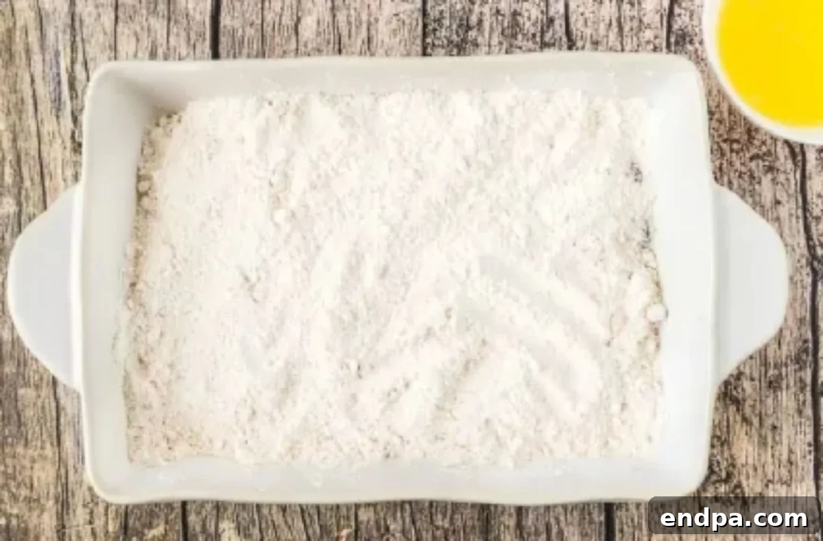 Dry yellow cake mix is evenly sprinkled over the layer of cherry pie filling in the baking dish.