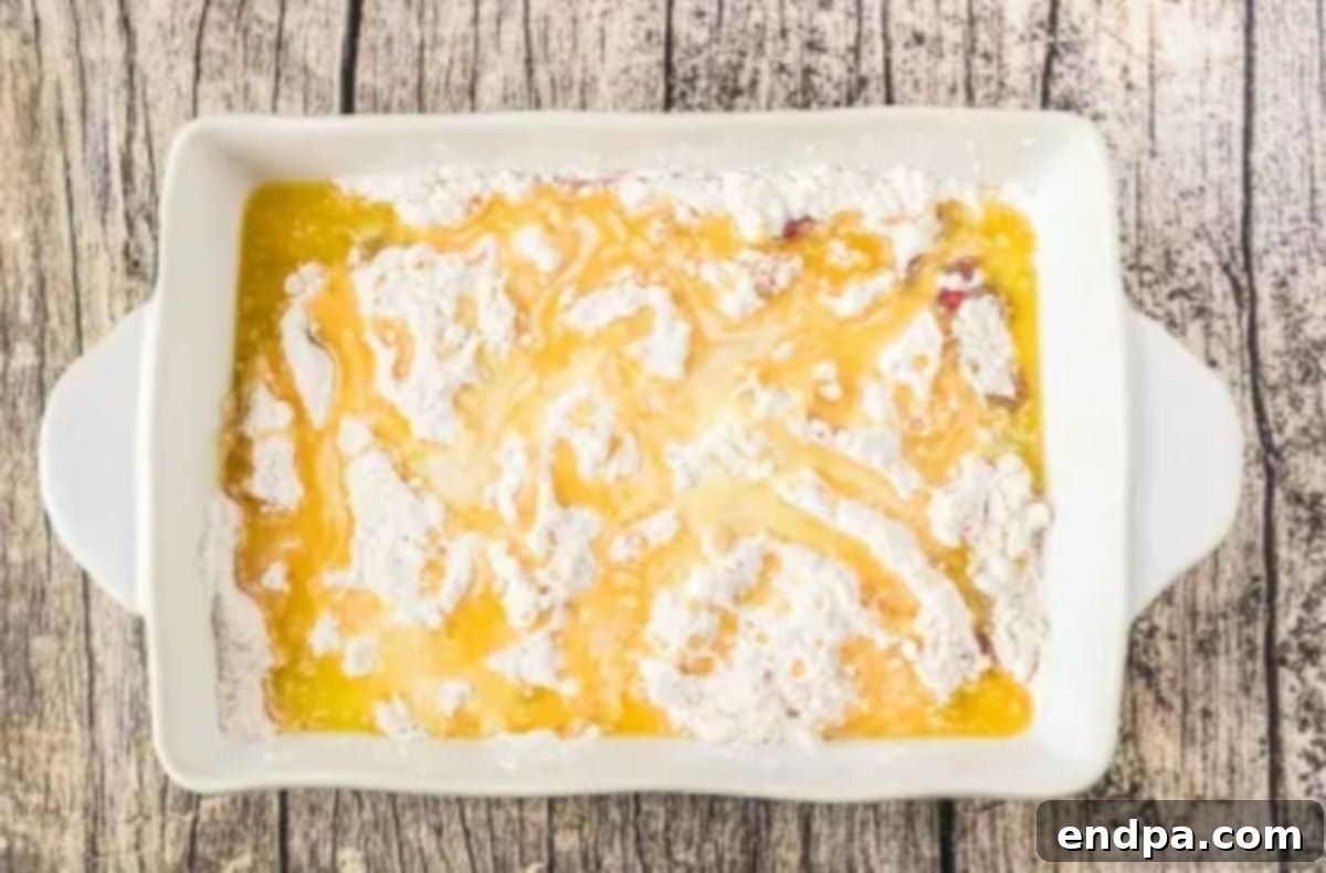 Melted butter is carefully drizzled over the dry cake mix layer in the baking dish, aiming to cover as much as possible.