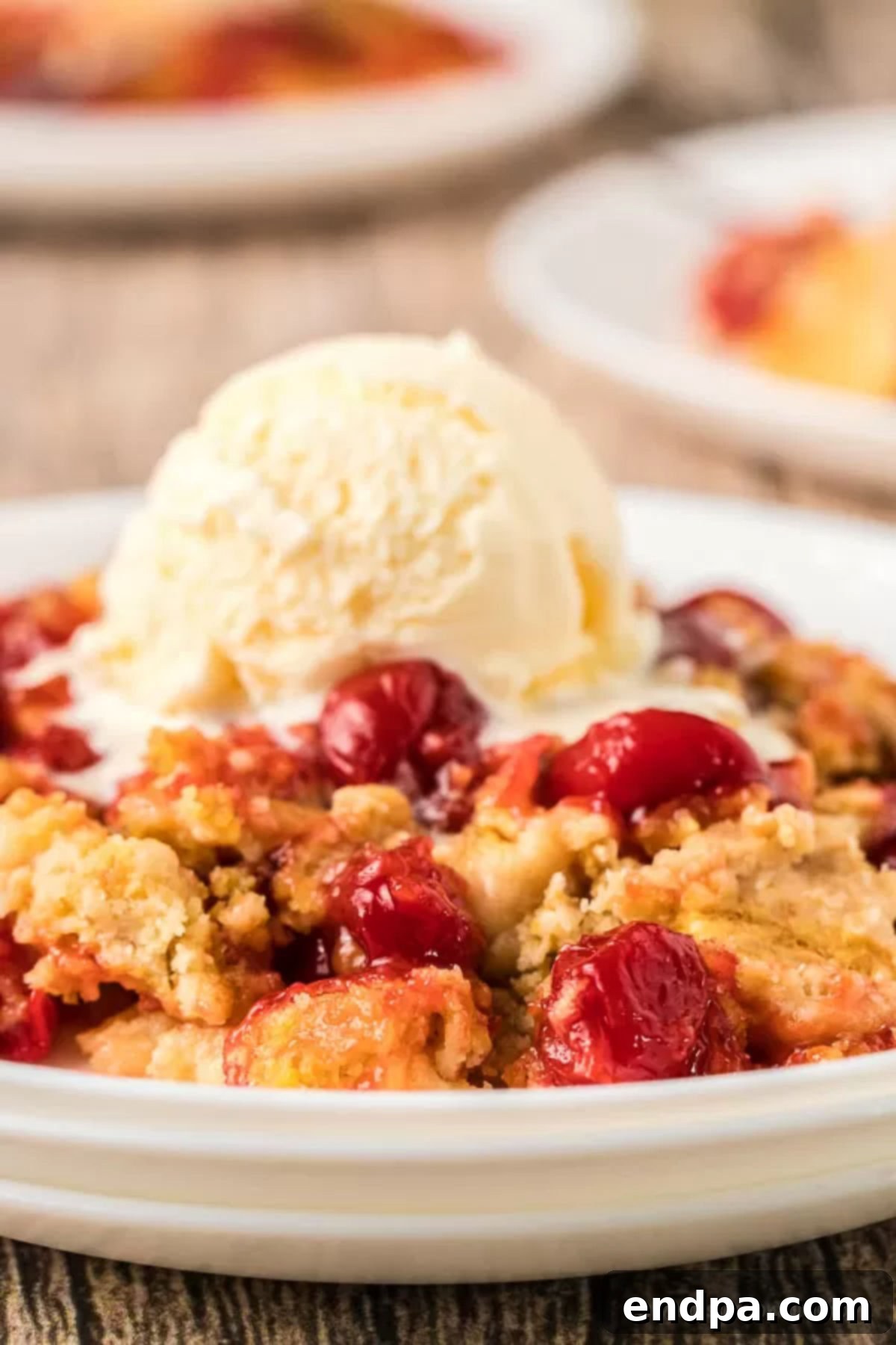 A serving of cherry dump cake on a plate, topped with a melting scoop of vanilla ice cream, and garnished with fresh mint.