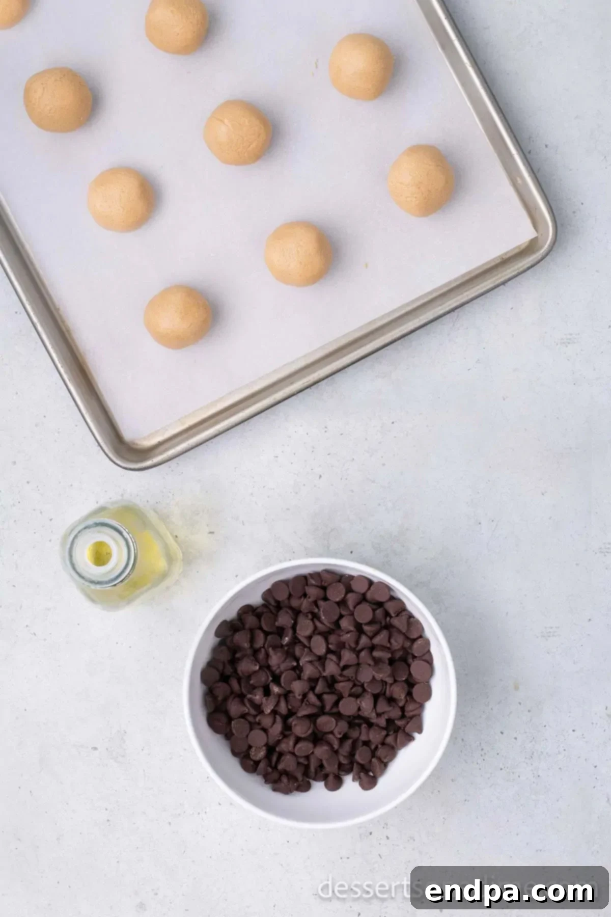 Buckeye Peanut Butter Delights 7 Neatly rolled peanut butter balls arranged on a baking sheet lined with wax paper, alongside a bowl of chocolate chips, ready for their second chill.
