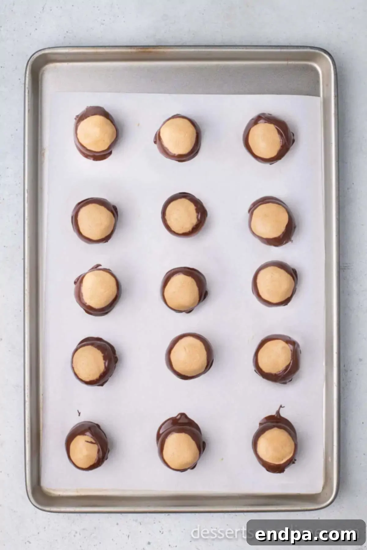 Buckeye Peanut Butter Delights 9 Freshly dipped Buckeye Peanut Butter Balls resting on a baking sheet lined with wax paper, with smooth chocolate coatings and visible peanut butter tops, chilling.