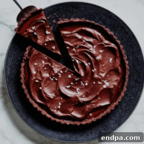 A stunning Salted Caramel Chocolate Tart, featuring a glossy chocolate layer over a rich caramel filling, served on a white plate.