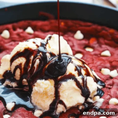 A warm, gooey Red Velvet Skillet Cookie, topped with melted white chocolate chips and a scoop of ice cream.