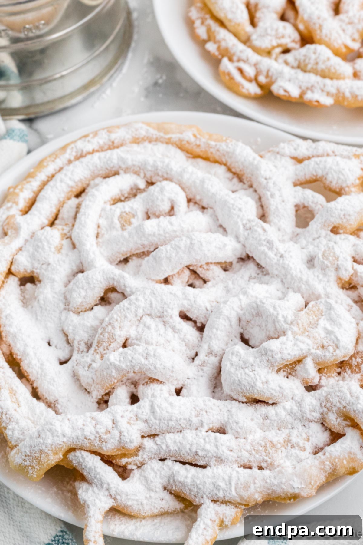 A close-up shot of a funnel cake generously coated with powdered sugar, highlighting its intricate crispy texture and inviting golden color.