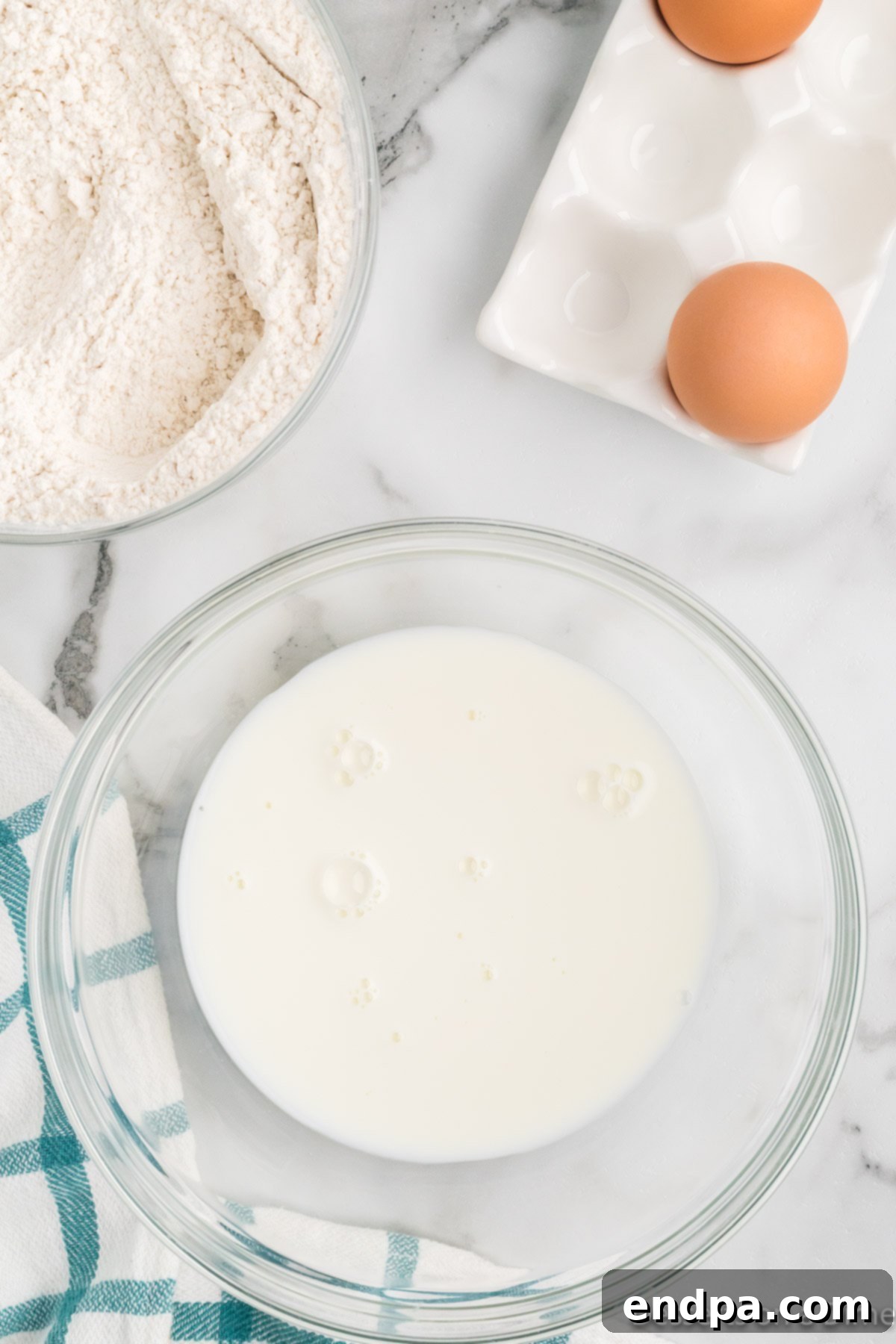 Wet ingredients for funnel cake batter, including milk and two large eggs, mixed in a separate bowl.