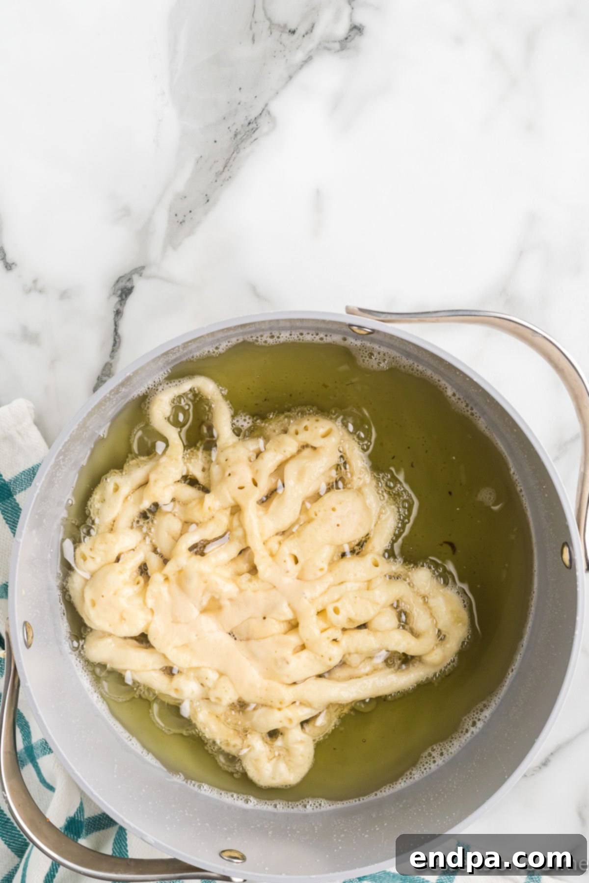 Funnel cake batter being drizzled from a funnel into hot oil in a frying pan, creating the classic crisscross pattern.