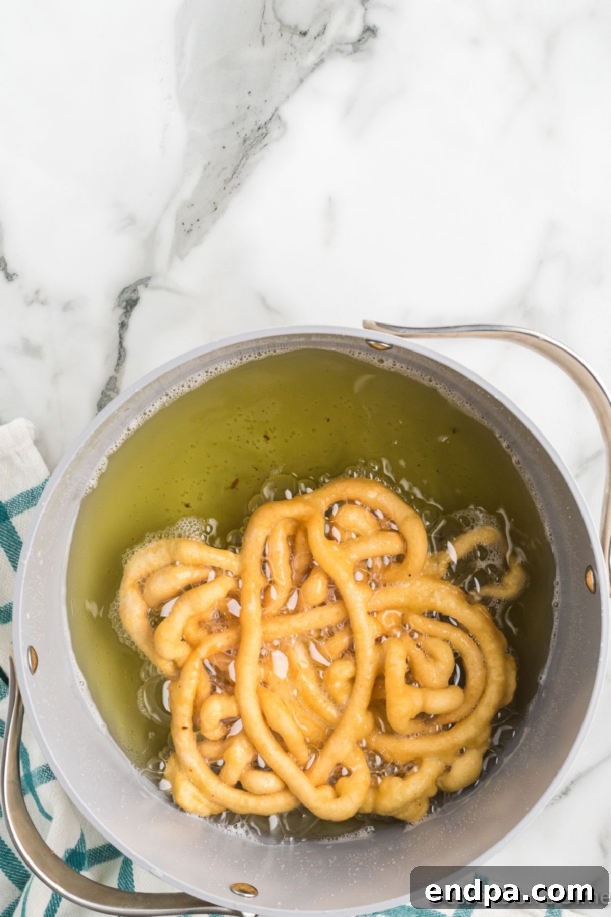 A funnel cake frying in hot oil, turning golden brown and achieving a crispy texture, indicating it's cooked to perfection.