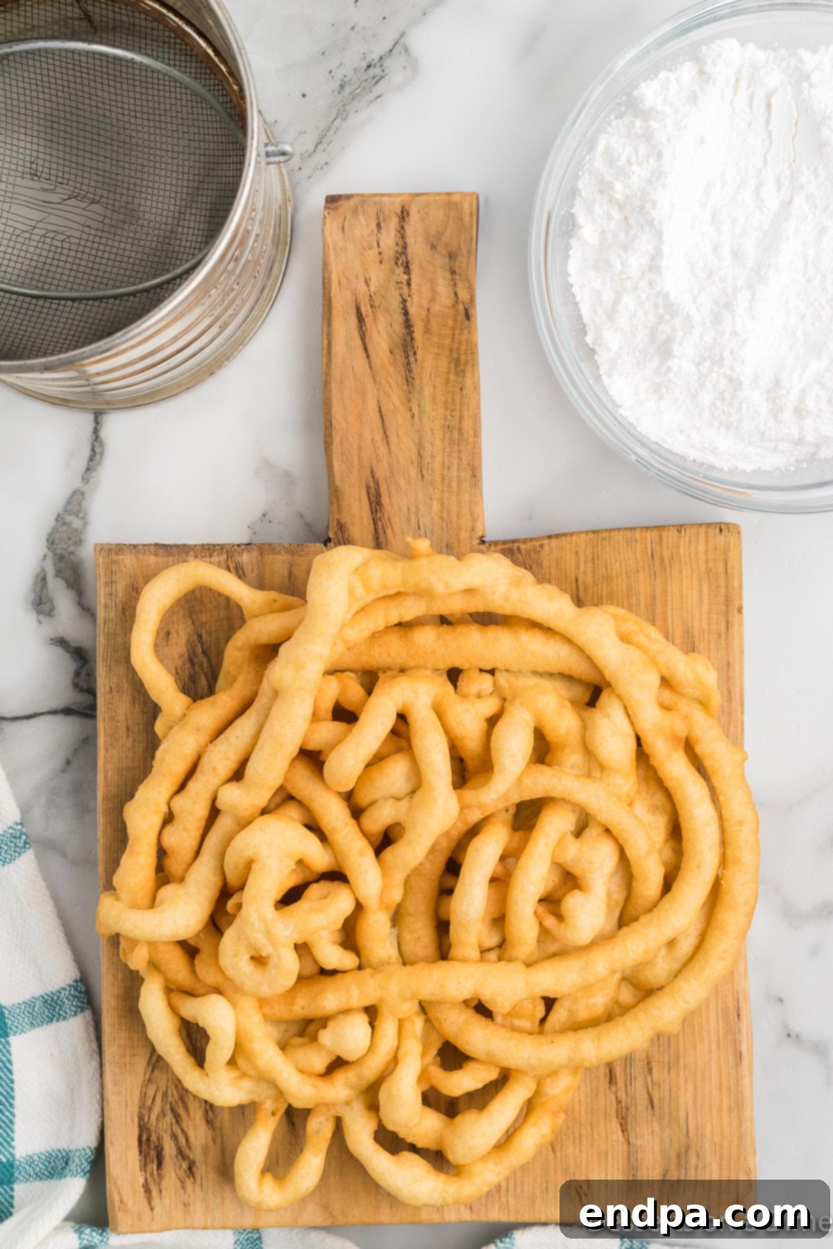 A freshly fried funnel cake, removed from the oil and placed on a paper towel-lined plate, ready for powdered sugar.