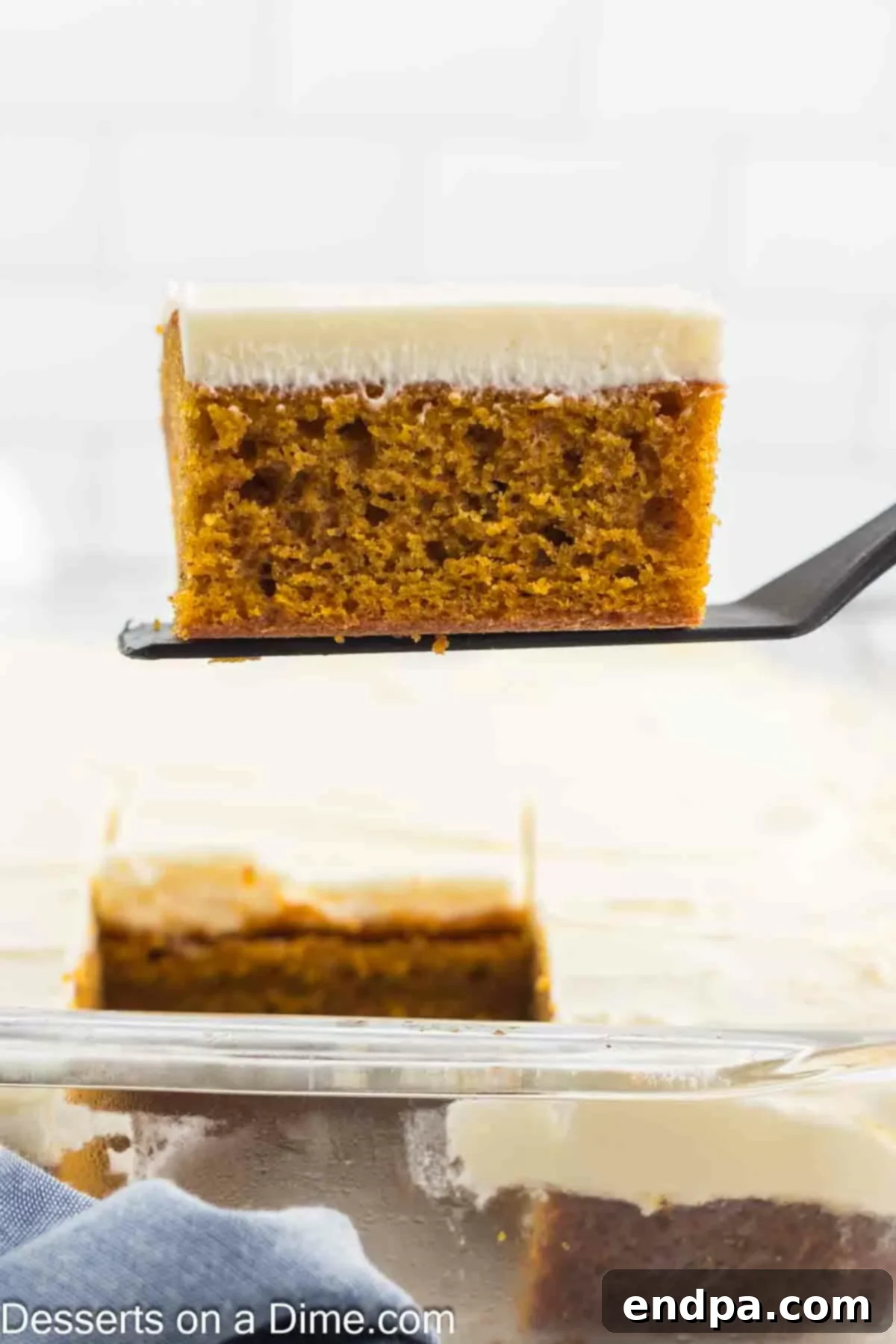 A golden-brown slice of freshly baked pumpkin cake is being gently lifted from the baking pan using a wide spatula. The image highlights the cake's tender, moist interior and showcases its readiness for the next delicious step: frosting.