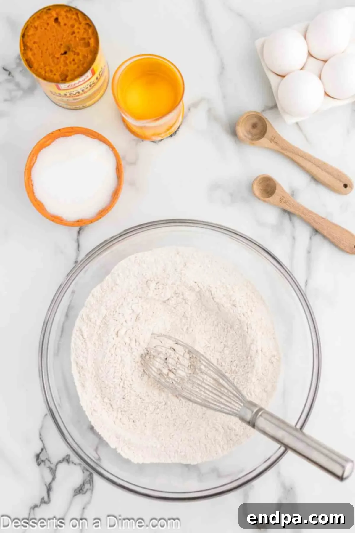 In a spacious mixing bowl, all the dry ingredients for the pumpkin cake—all-purpose flour, baking powder, baking soda, fragrant pumpkin pie spice, and a pinch of salt—are being meticulously whisked together, ensuring an even distribution of every component.