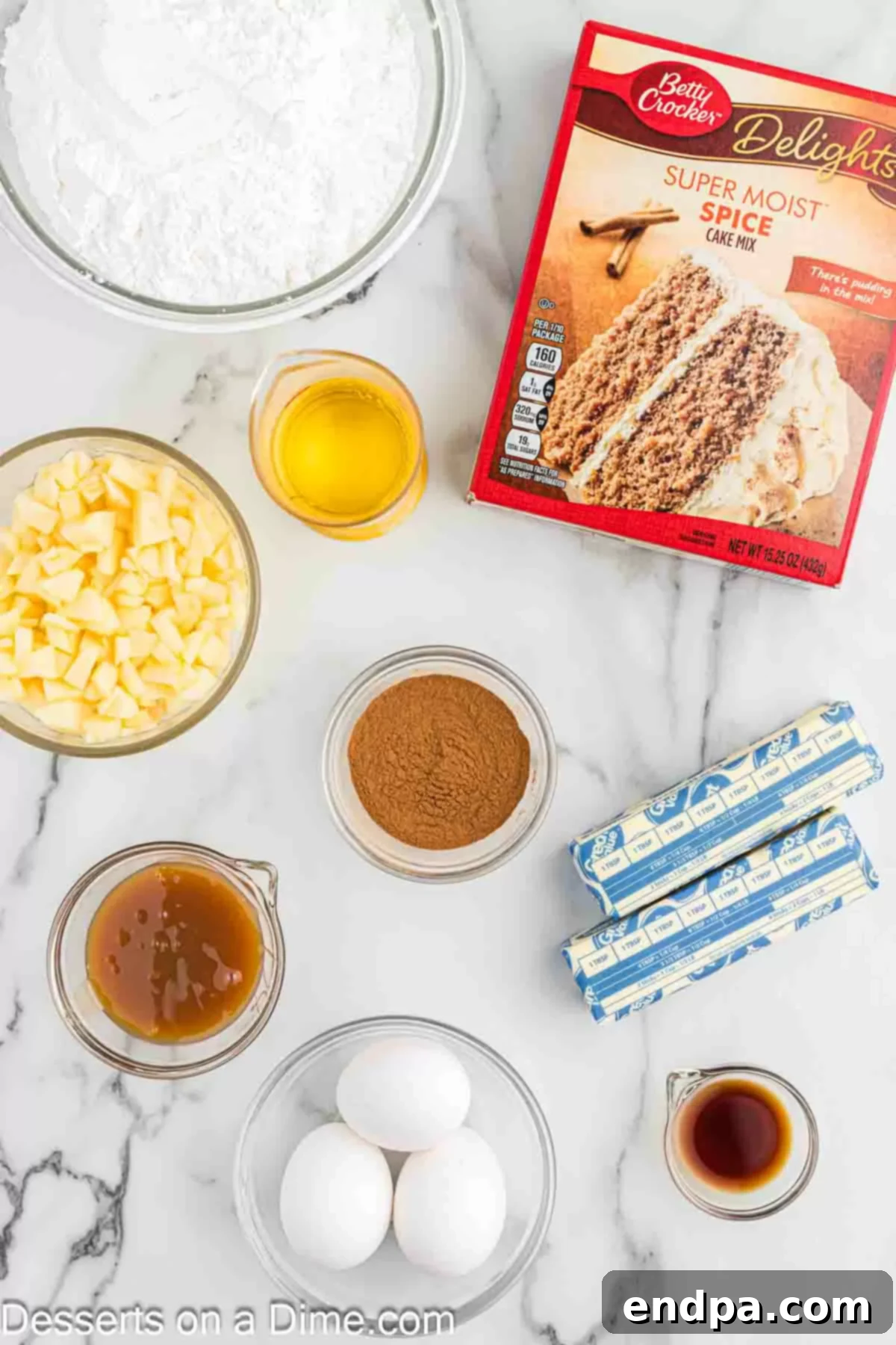 Sticky Caramel Apple Swirl Cupcakes 3 Ingredients for caramel apple cupcakes laid out: spice cake mix, eggs, oil, chopped apples, butter, caramel sauce, powdered sugar, and cinnamon.