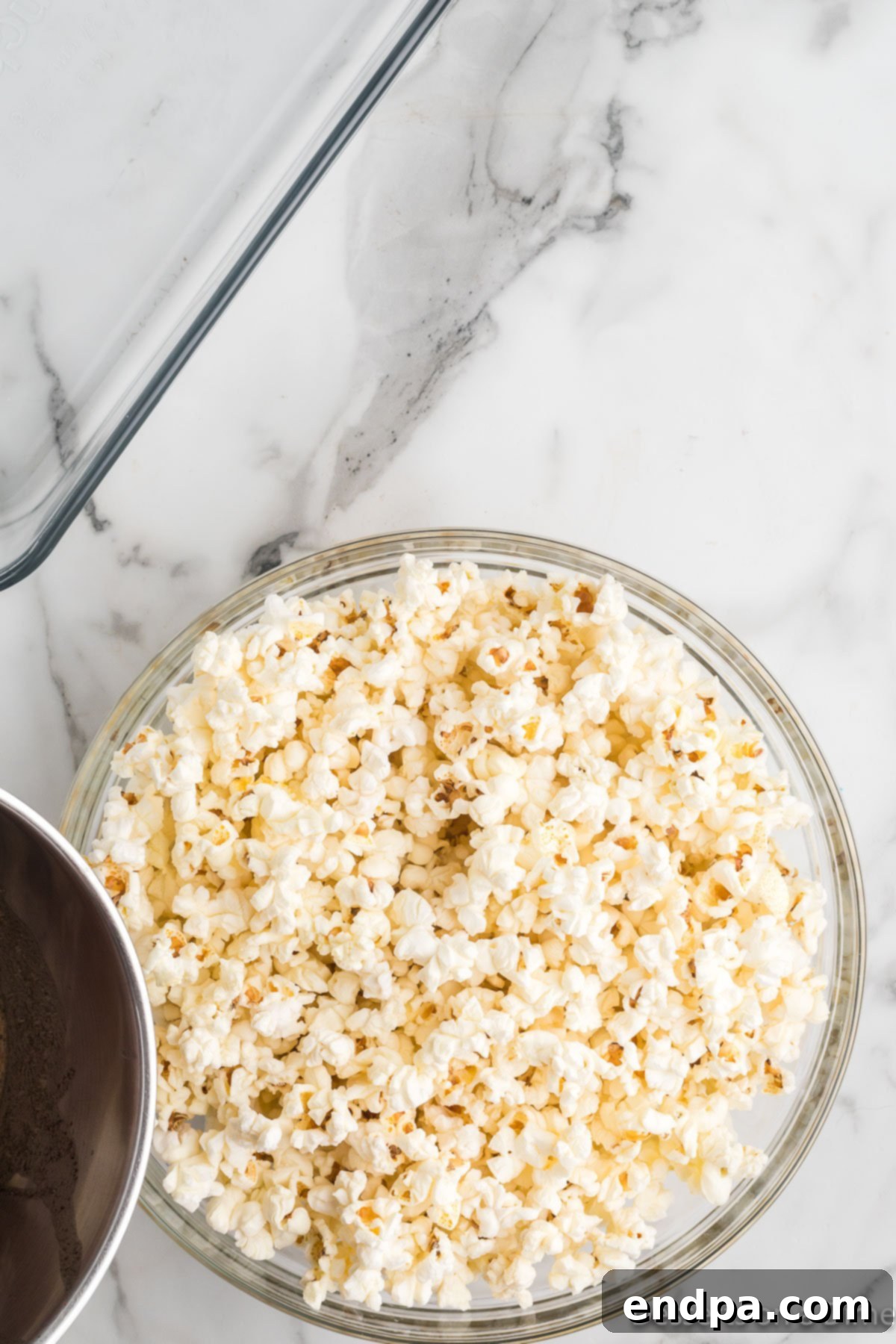 The butter and spice mixture being poured over popped popcorn in a large bowl.