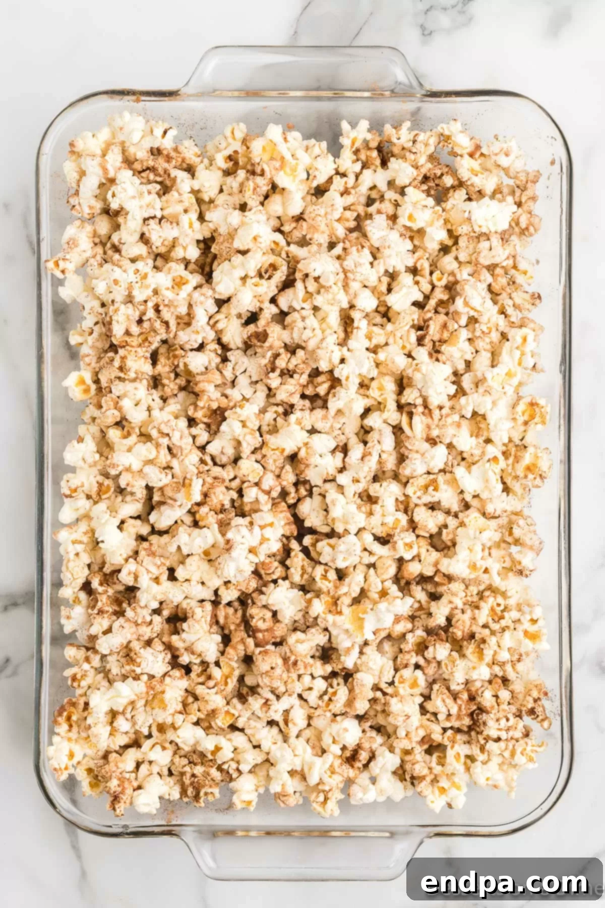 Pumpkin spice popcorn mixture spread out in a baking dish, ready for the oven.