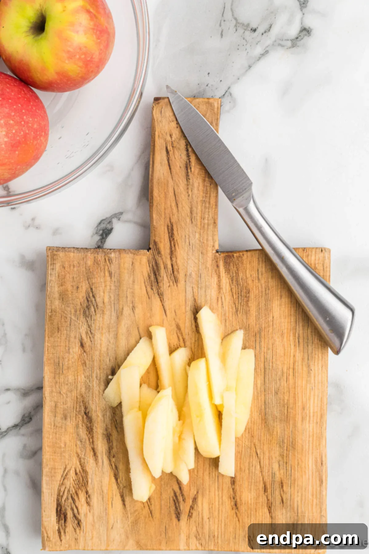 Fresh apples peeled, cored, and sliced into fry-like strips on a wooden cutting board.