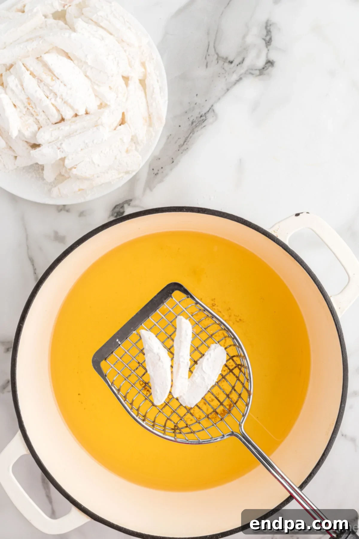 Cornstarch-coated apple fries carefully being placed into hot oil for frying.