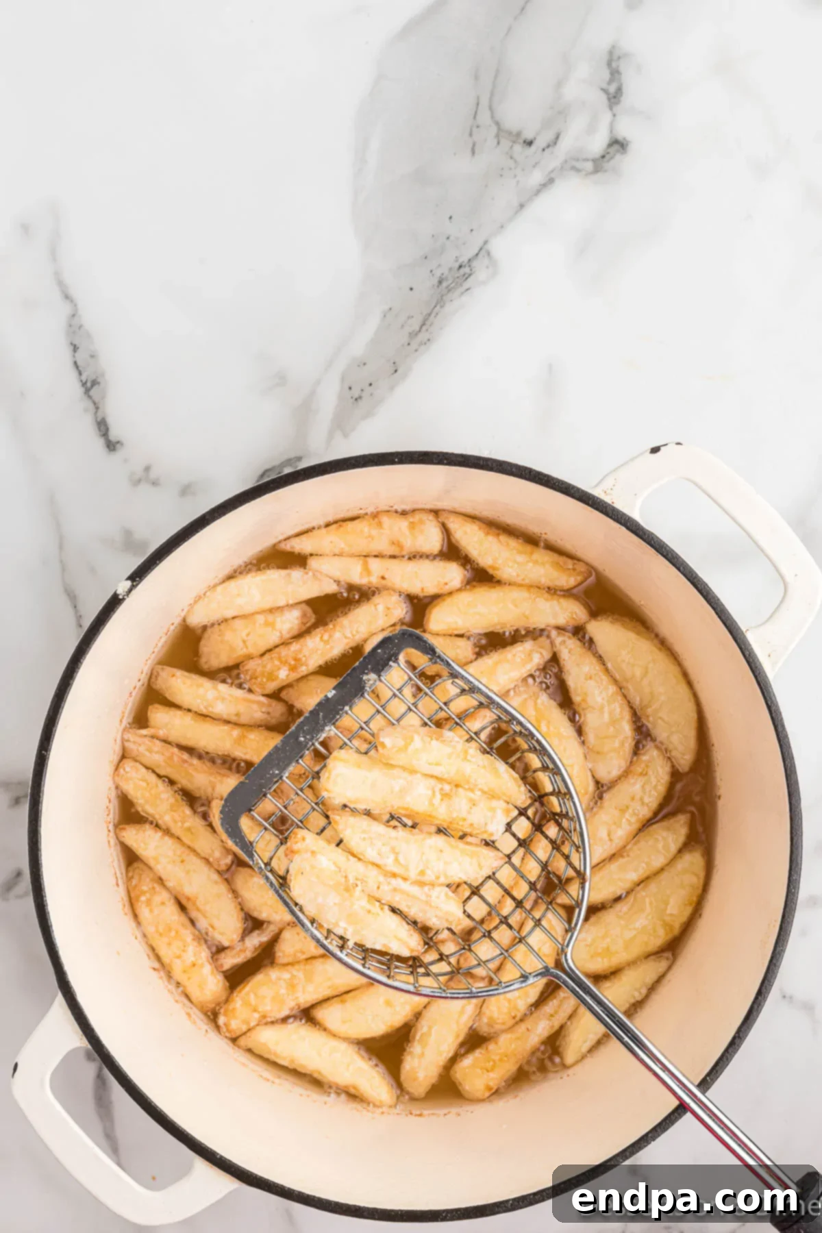 Apple fries being turned over in the hot oil to ensure even cooking and browning.