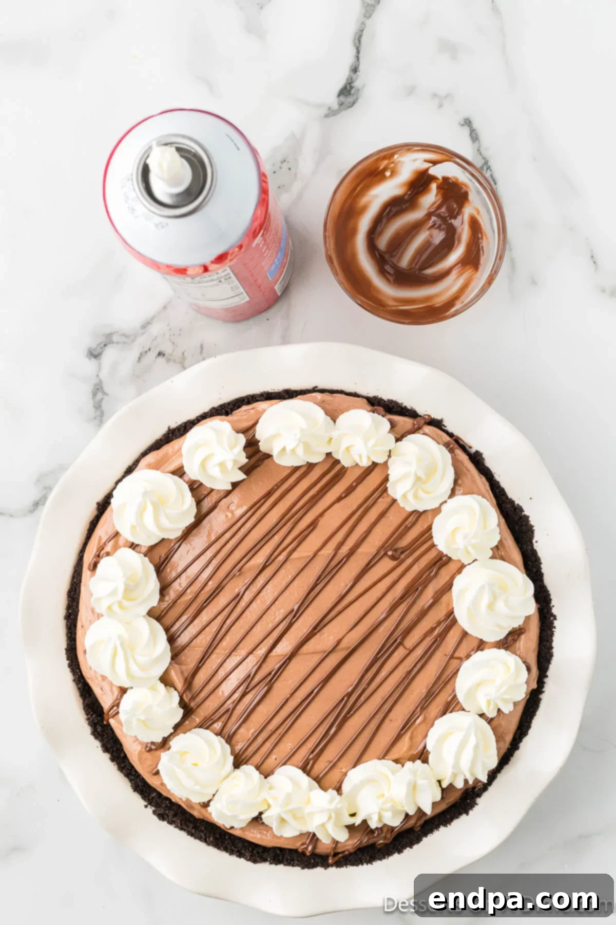 Decadent No Bake Nutella Cheesecake 11 A fully assembled No Bake Nutella Cheesecake, drizzled with melted Nutella and adorned with whipped cream dollops around the edge, ready to be sliced and served.