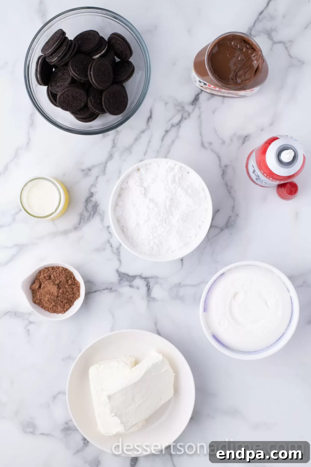 Decadent No Bake Nutella Cheesecake 3 A selection of ingredients laid out for making a no-bake Nutella cheesecake, including Oreo cookies, sticks of butter, blocks of cream cheese, a jar of Nutella, cocoa powder, powdered sugar, and a container of whipped topping.
