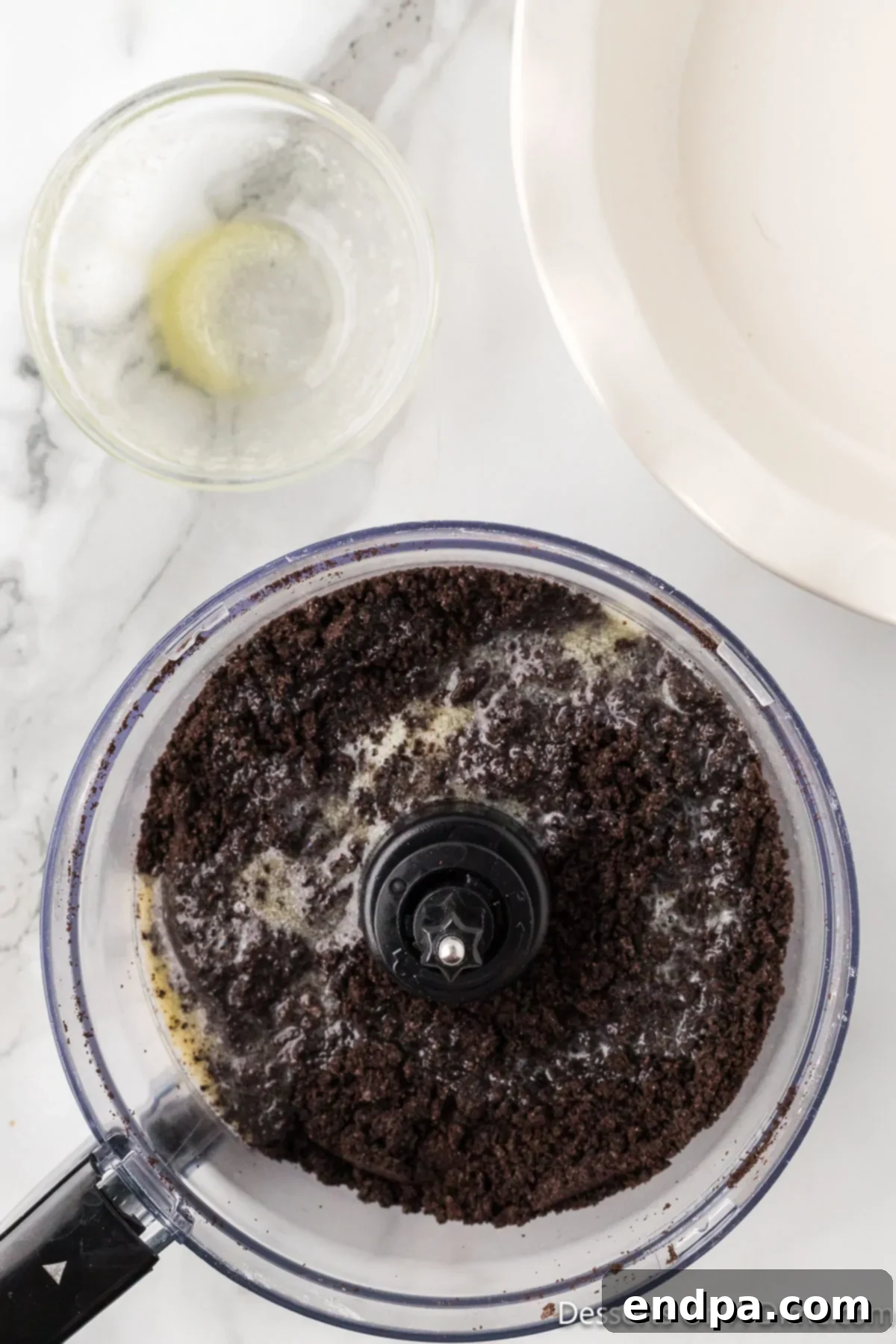 Decadent No Bake Nutella Cheesecake 5 Melted butter being mixed into crushed Oreo cookie crumbs in a glass bowl to form the cheesecake crust.