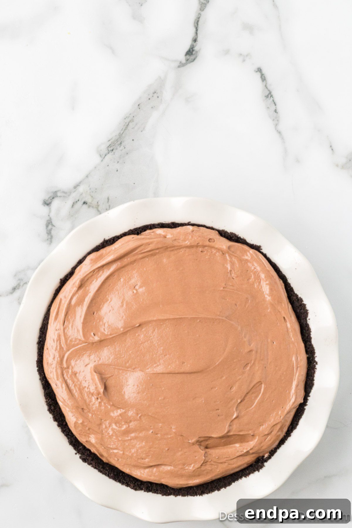 Decadent No Bake Nutella Cheesecake 10 The smooth Nutella cheesecake filling spread evenly into the chilled Oreo cookie crust in a pie plate, ready for refrigeration.