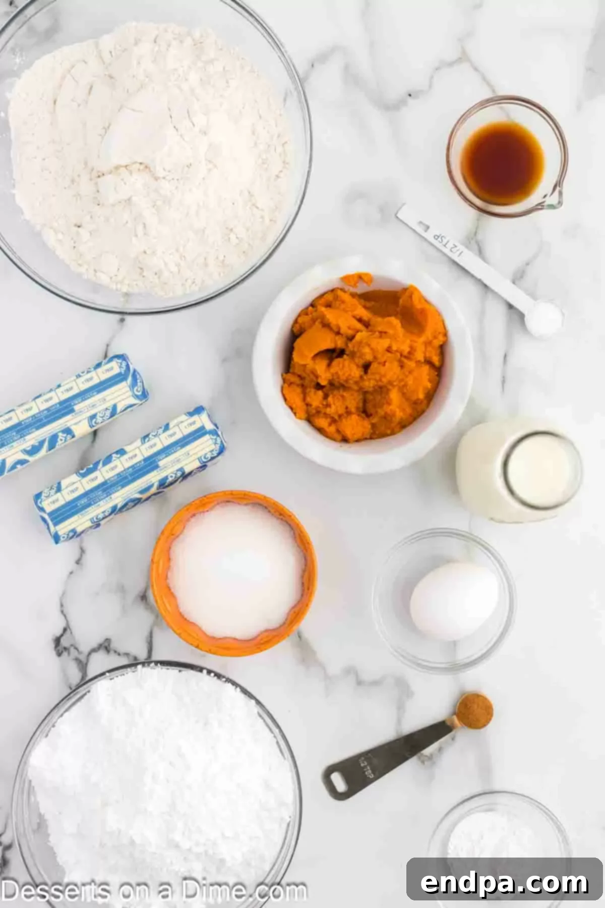 A flat lay photograph showcasing all the fresh ingredients required for baking Pumpkin Sugar Cookies, including flour, baking powder, sugar, softened butter, eggs, pumpkin puree, powdered sugar, milk, and pumpkin pie spice, neatly arranged.