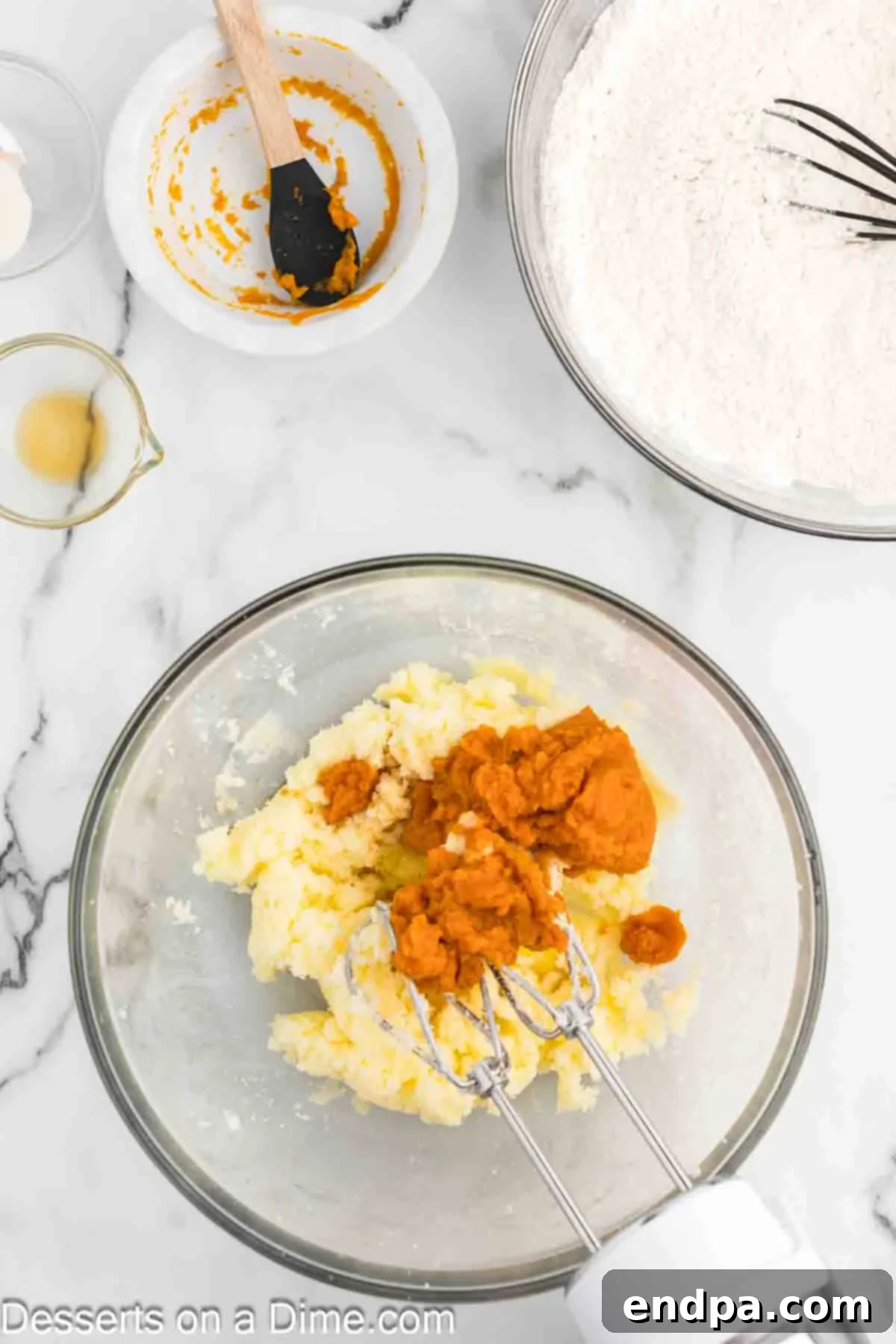 Vanilla extract, a large room-temperature egg, and pure pumpkin puree being added to the creamed butter and sugar mixture in a mixing bowl.