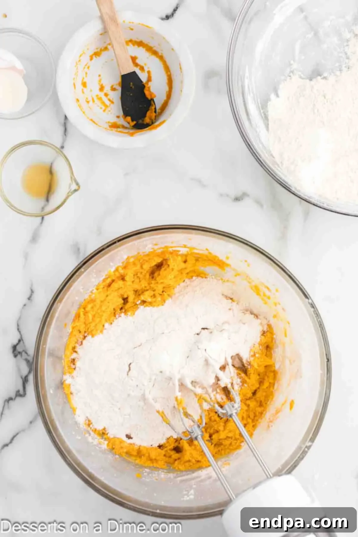 The dry flour mixture being gradually added to the wet butter and pumpkin mixture in a stand mixer, forming a cohesive cookie dough.