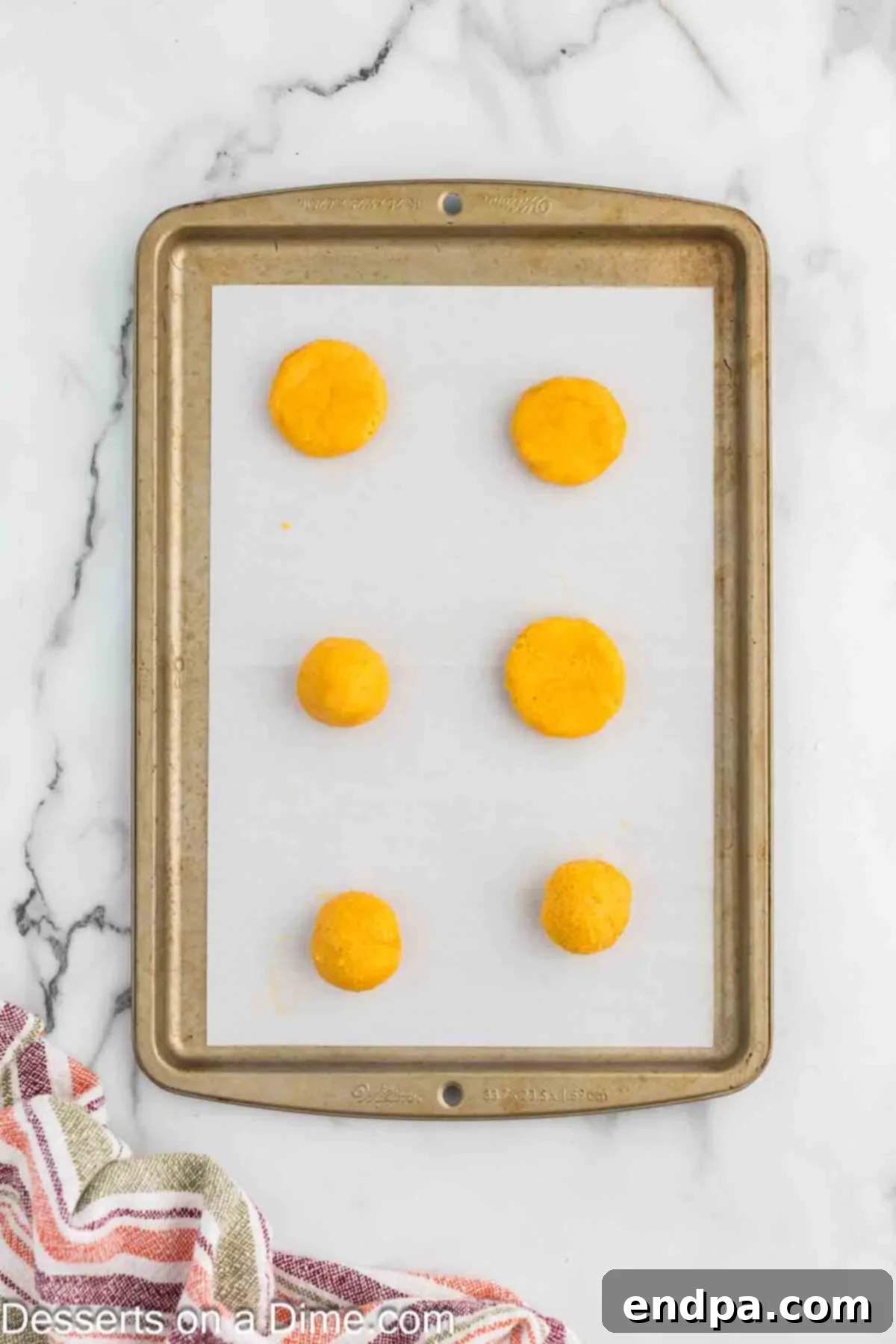 Cookie dough balls being gently pressed down with the bottom of a glass on a parchment-lined baking sheet before baking, ensuring even thickness.
