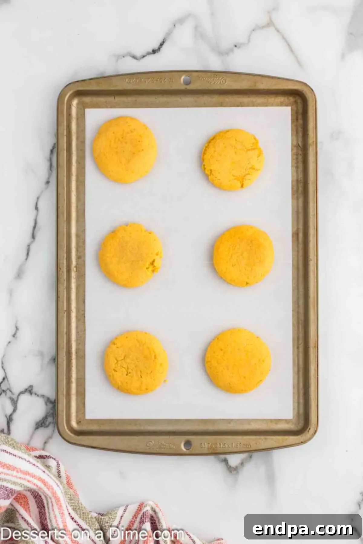 Pumpkin sugar cookies arranged neatly on a baking sheet, ready to be placed into the oven for baking, showcasing their uniform size.