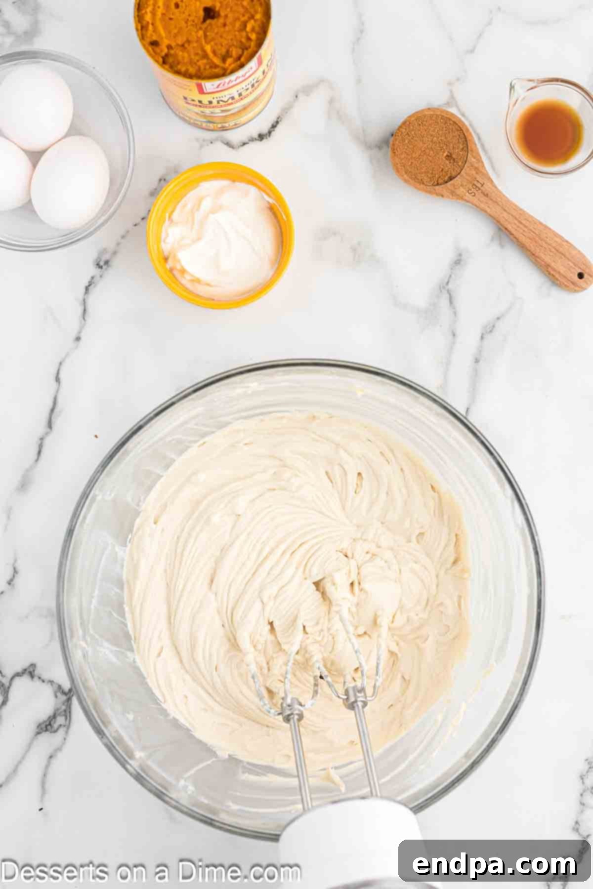 Velvet Pumpkin Spice Cheesecake 4 A mixing bowl containing softened cream cheese and brown sugar being beaten together with an electric hand mixer, creating a light and fluffy texture.