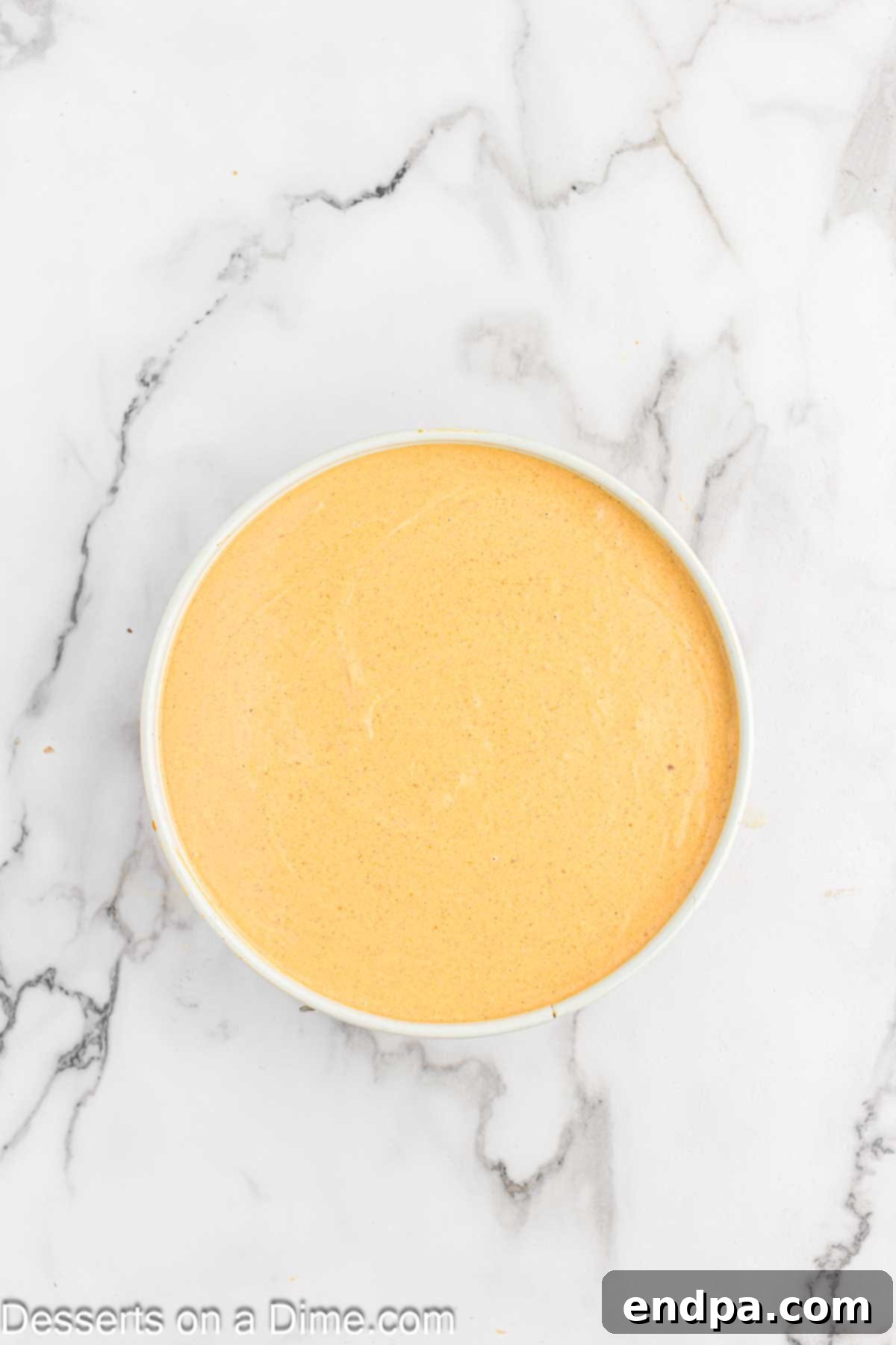 Velvet Pumpkin Spice Cheesecake 6 Smooth pumpkin cheesecake batter being poured into a pre-baked graham cracker crust in a springform pan, ready for the water bath and baking process.